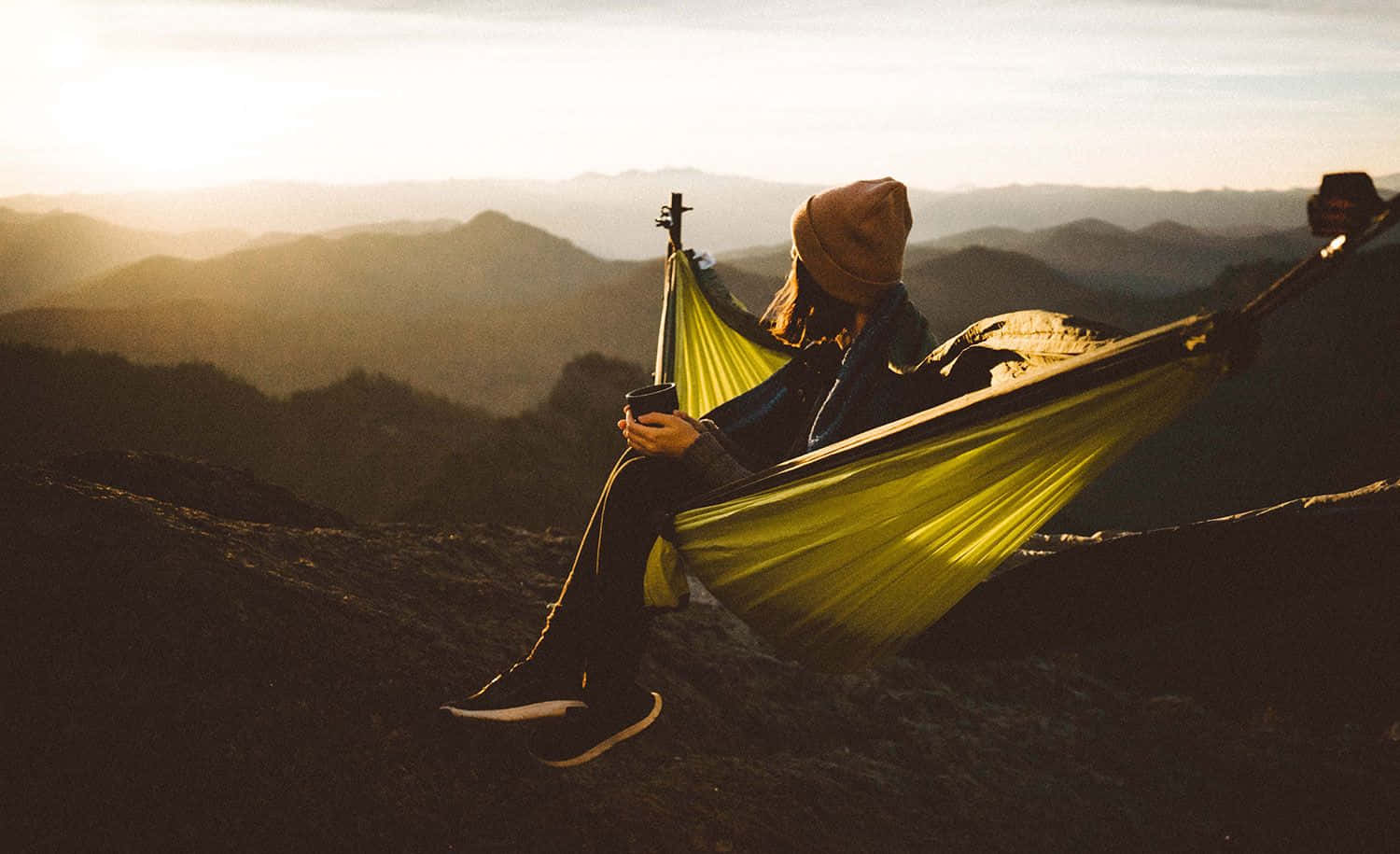 Minimalist Camping 桌布 壁紙 — 一個戴著毛帽的人在金色時刻，於懸掛在山脊上的亮黃色吊床上放鬆。