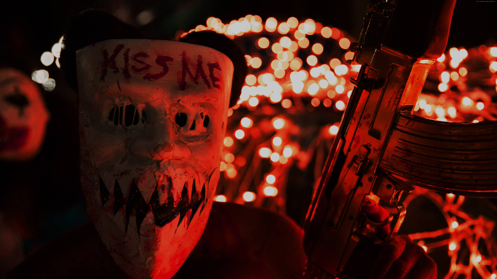 Purge 桌布 壁紙 — 一個戴著沾血面具、上面寫著「KISS ME」的人，在夜晚以發光的紅燈為背景，手持步槍。