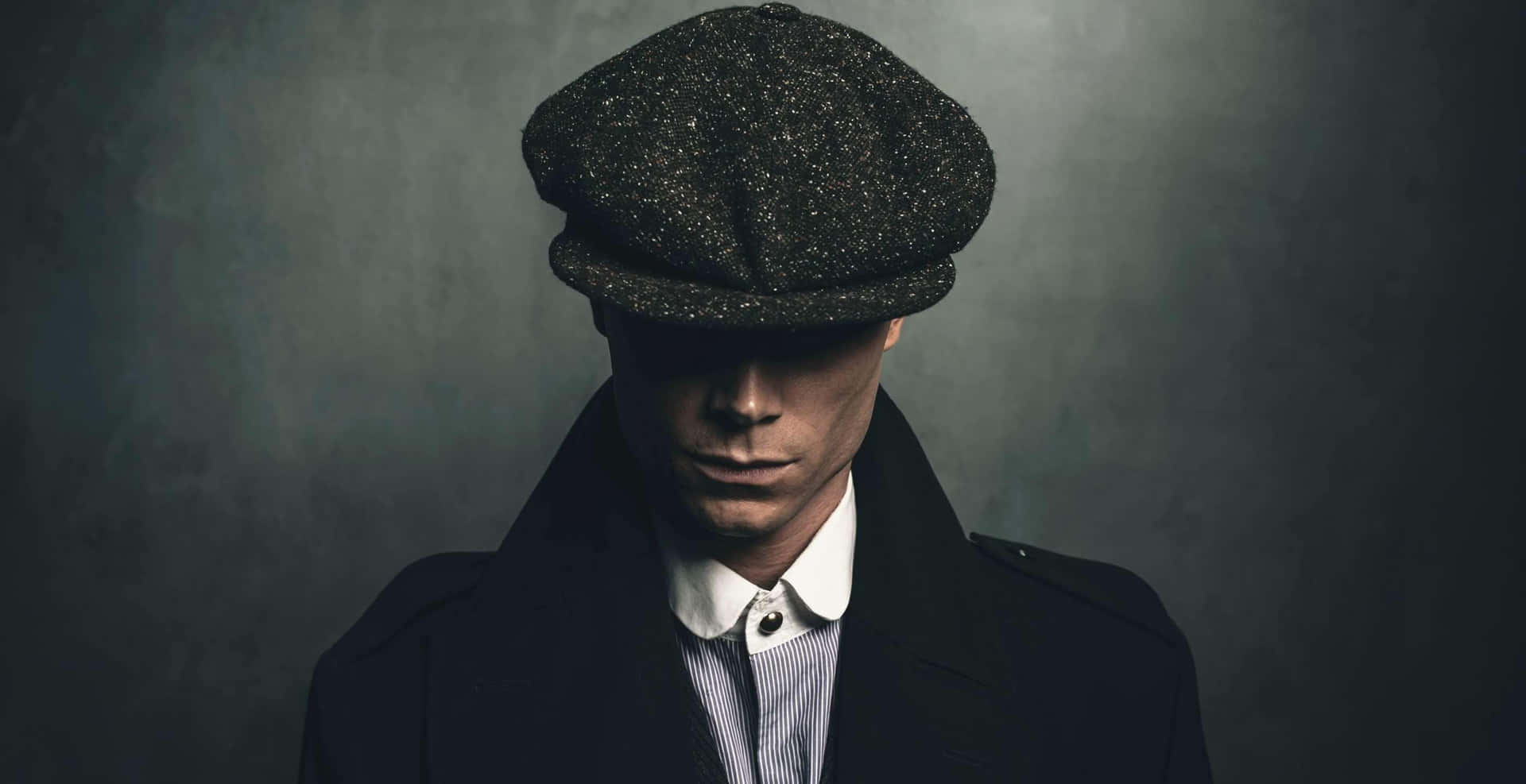 一個戴著平頂帽和外套的男人，在灰色背景前表情嚴肅。 — Peaky Blinders 壁紙