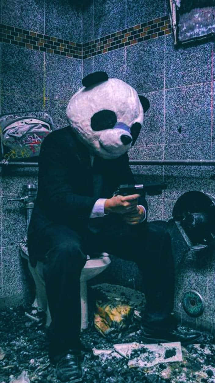 一個戴著熊貓面具的人坐在馬桶上，在骯髒的浴室裡手持一把槍。 — 槍枝 GIF 壁紙