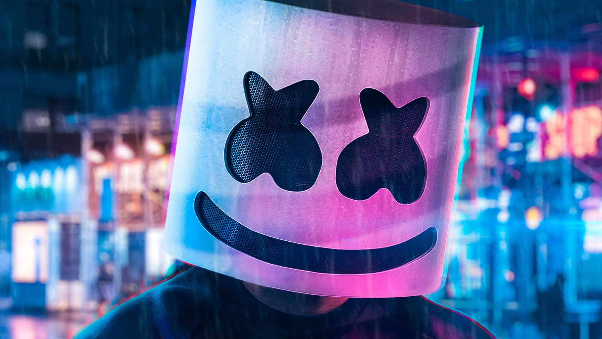 Marshmello 動態圖 桌布 壁紙 — 一個戴著發光Marshmello面具的人，夜晚站在被雨水浸透、霓虹燈閃爍的城市街道上。