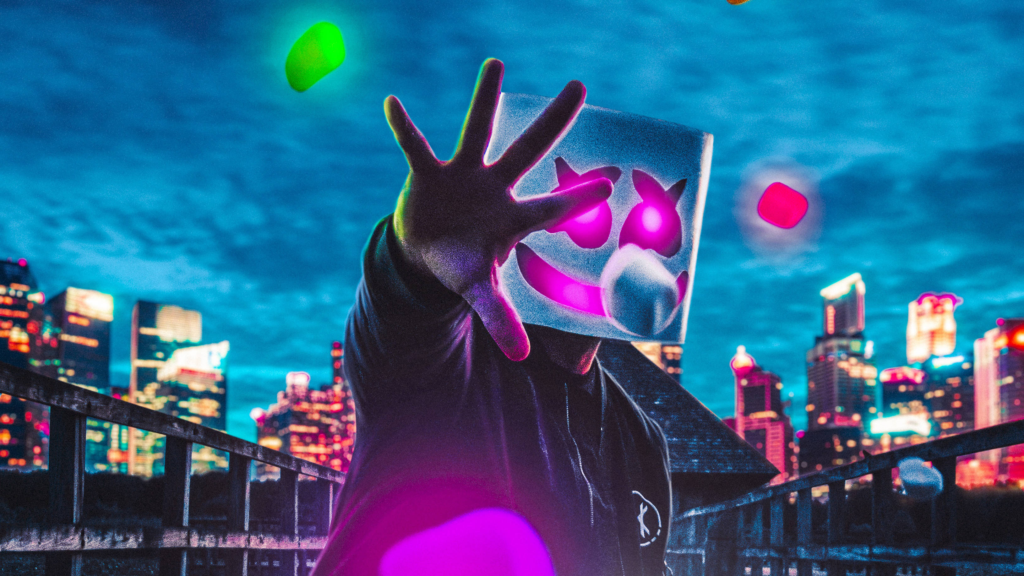 Marshmello 4K 桌布 壁紙 — 一個戴著發光粉紅色面具的人，在夜晚對著霓虹燈照亮的天際線舉起一隻手。