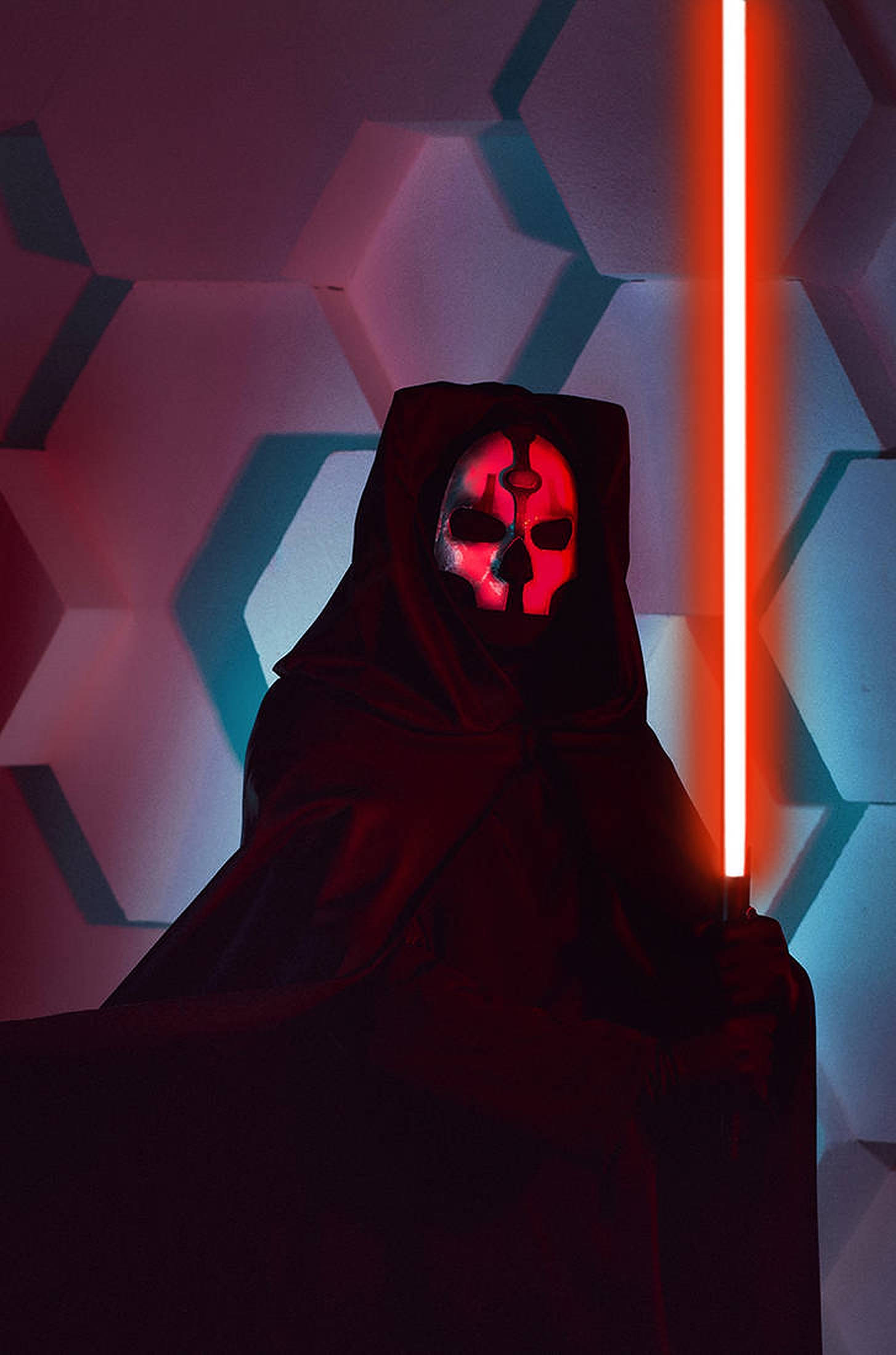 Darth Nihilus 桌布 壁紙 — 一個戴著發光紅色骷髏面具的兜帽人物，手持垂直的紅色光劍，面向以霓虹紅和藍色照亮的六角形牆壁。