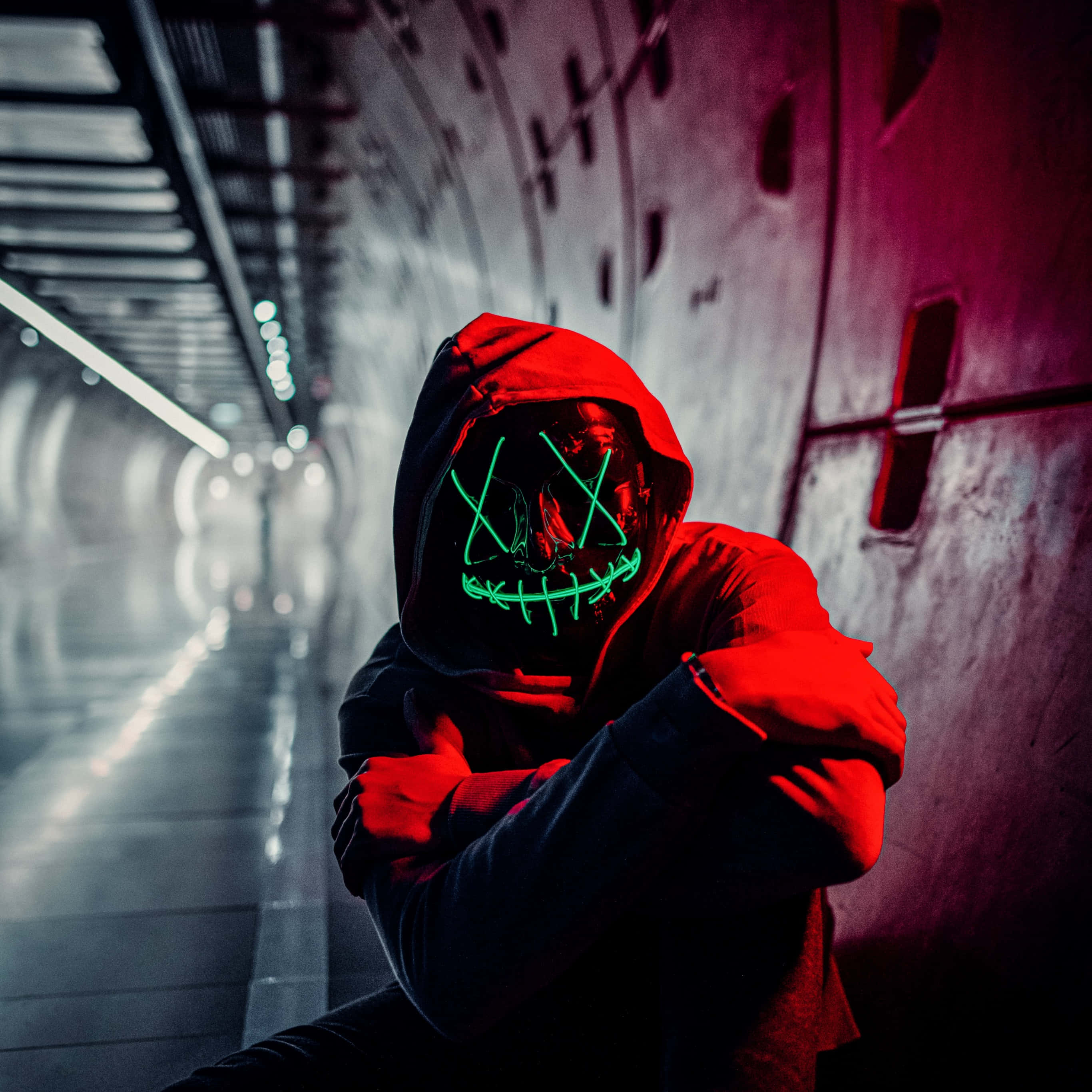 Mask 桌布 壁紙 — 一個戴著發光綠色骷髏面具的兜帽人物蹲在光線昏暗的工業隧道中。