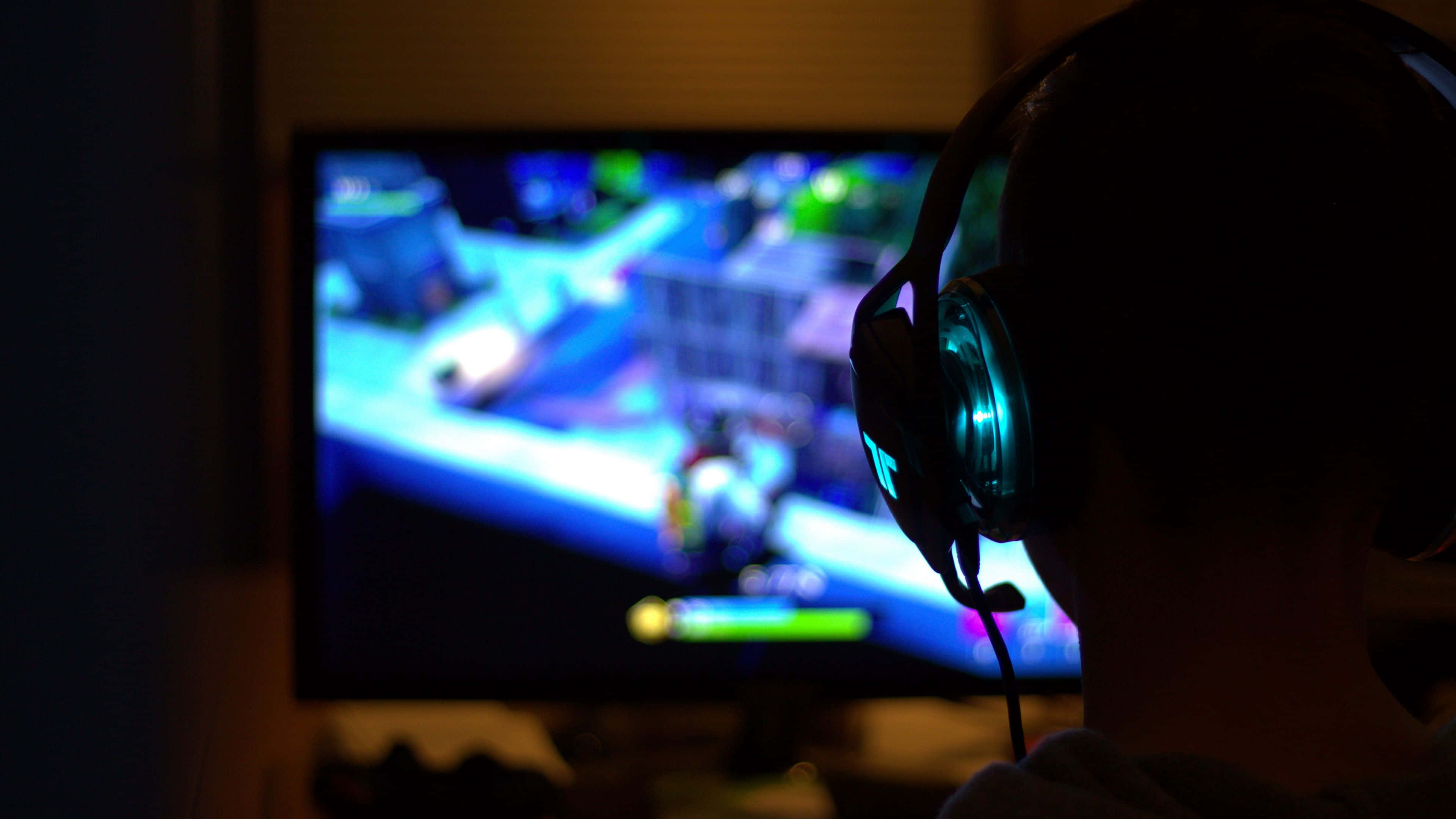 Dark Gaming 桌布 壁紙 — 一個戴著發光耳機的遊戲玩家剪影，在昏暗的房間中專注於充滿活力的藍色和綠色電玩遊戲螢幕。