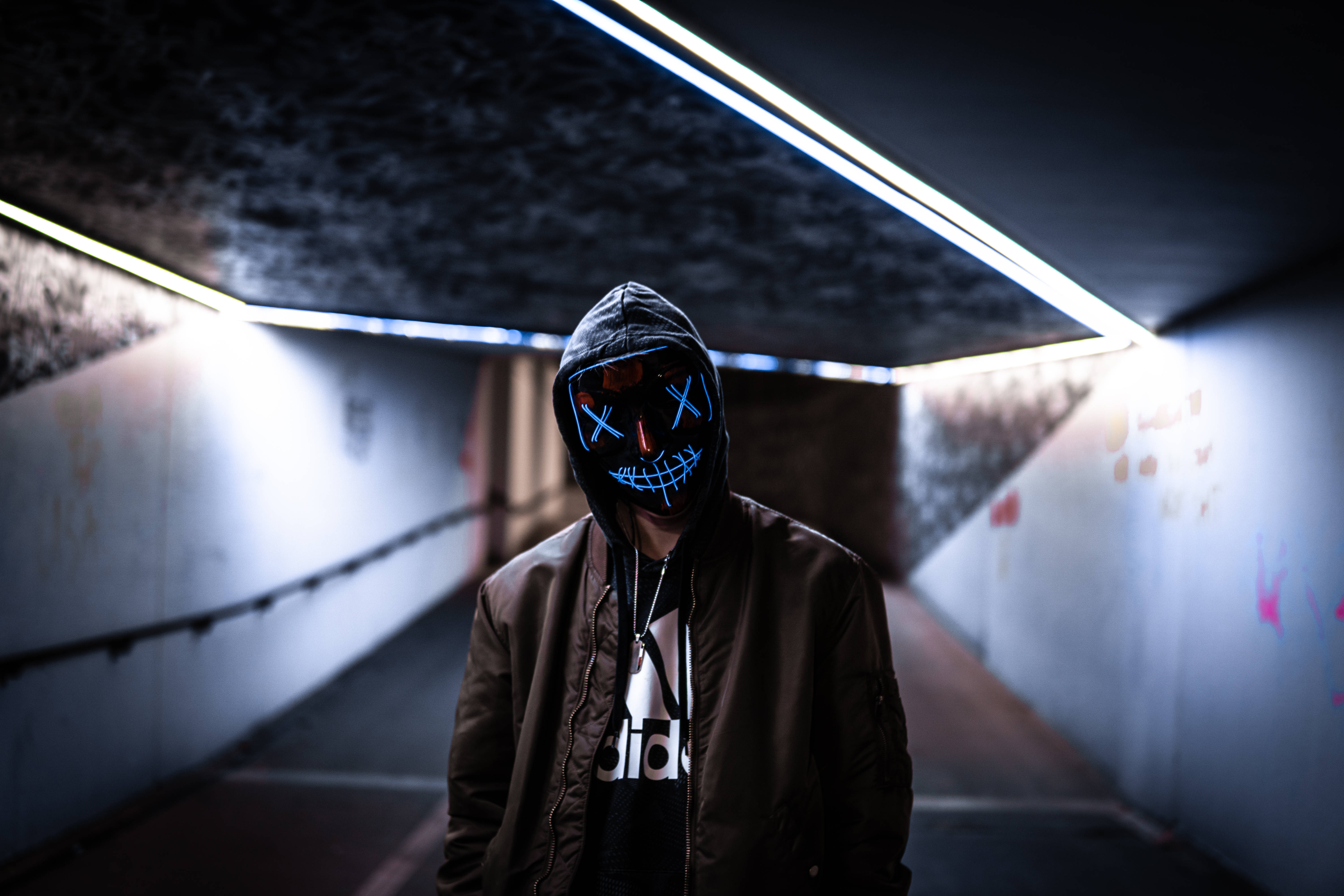 The Purge 桌布 壁紙 — 一個戴著發光藍色LED面具的人站在光線昏暗的城市隧道中，周圍是刺眼的螢光燈照明。