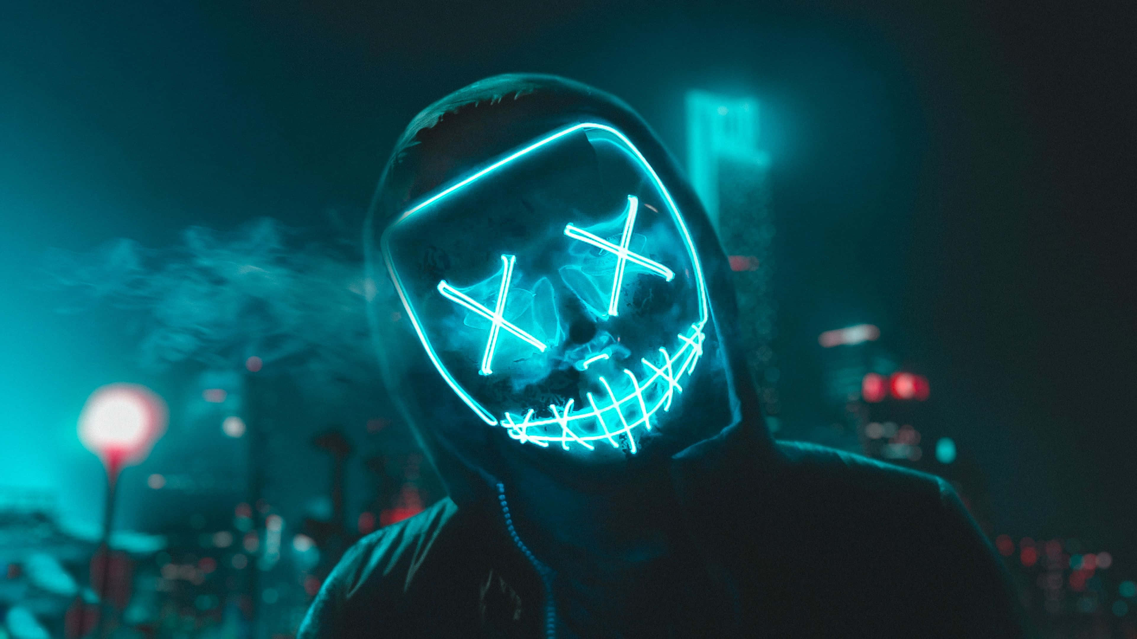 Neon Mask 桌布 壁紙 — 一個戴著發光藍色LED骷髏面具的人，在夜晚霓虹燈照亮的城市景觀中呼出煙霧。