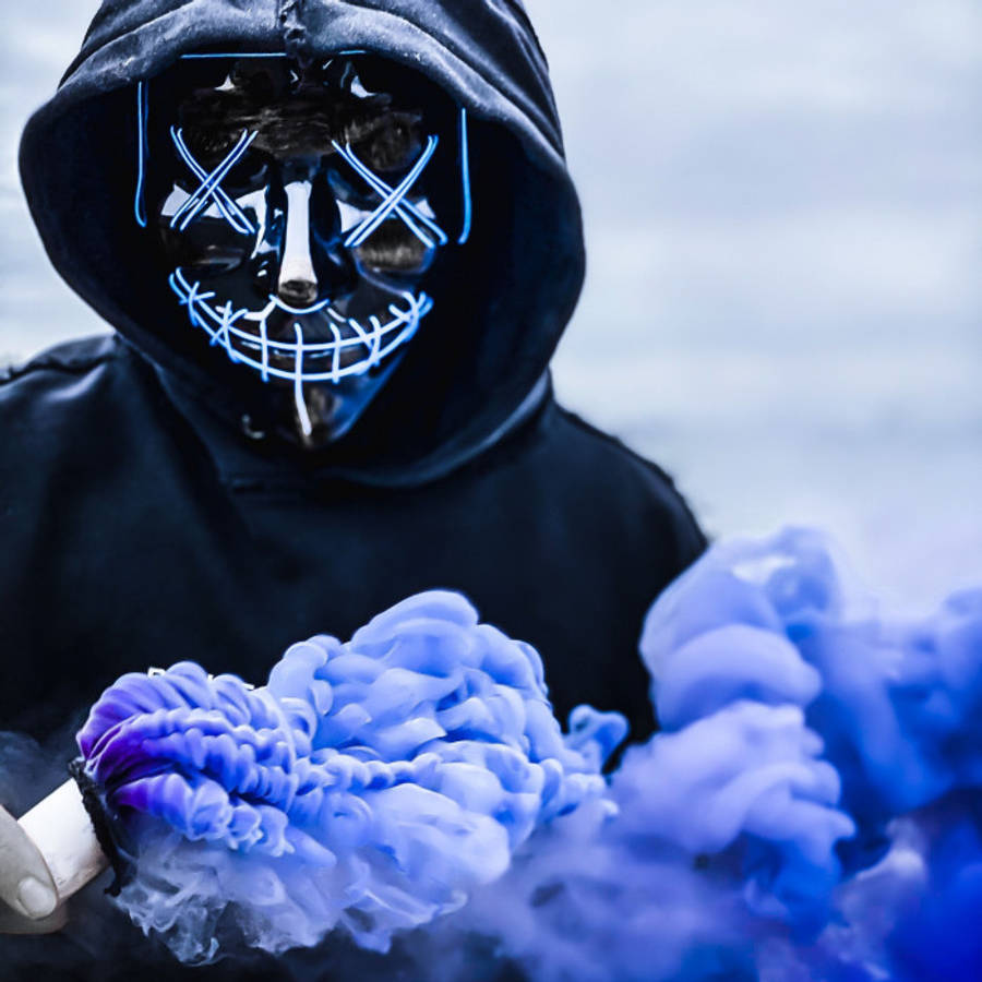 hacker 3d 桌布 壁紙 — 一個戴著發光藍色骷髏面具的兜帽人物，手持一個冒煙裝置，在陰雲密布的天空下釋放出鮮豔的藍色和紫色煙霧。
