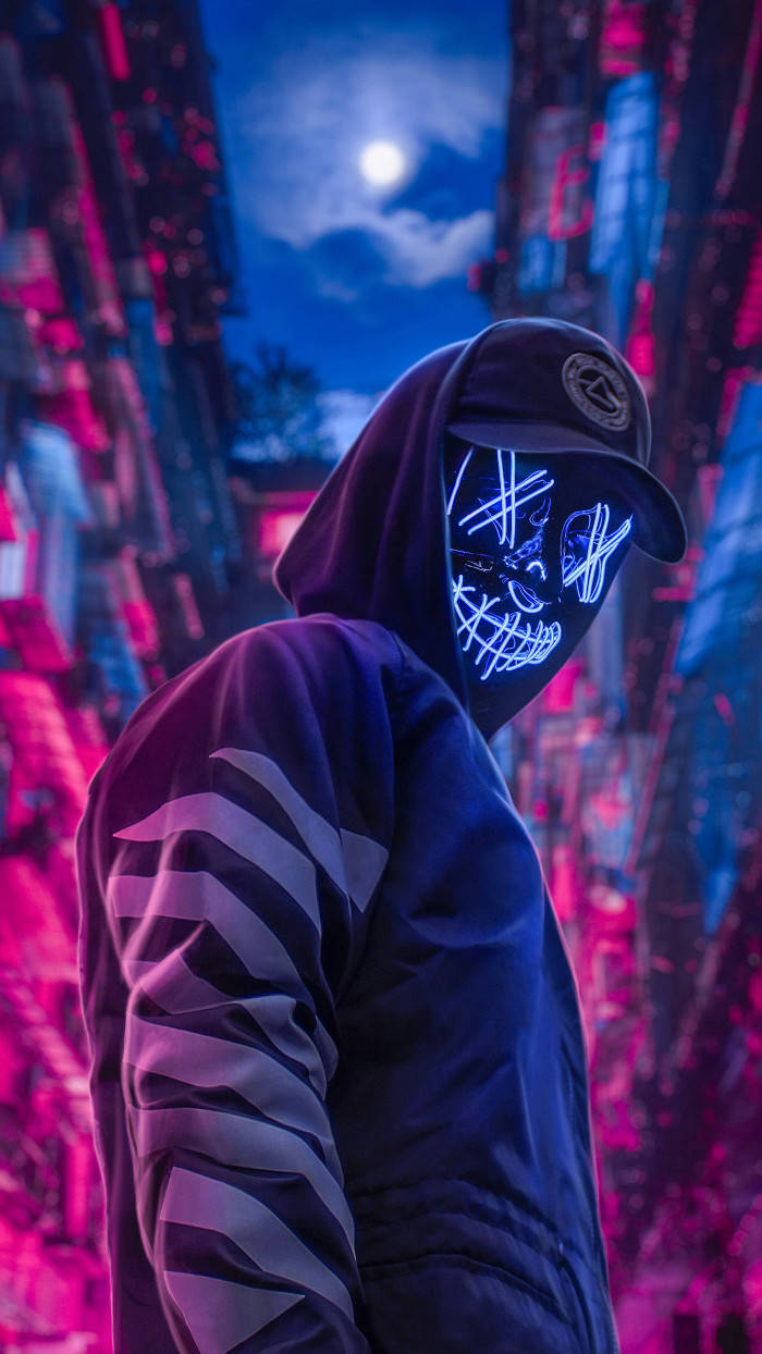hacker 3d 桌布 壁紙 — 一個戴著發光霓虹骷髏面具的兜帽人物站在滿月下的賽博龐克城市景觀中。
