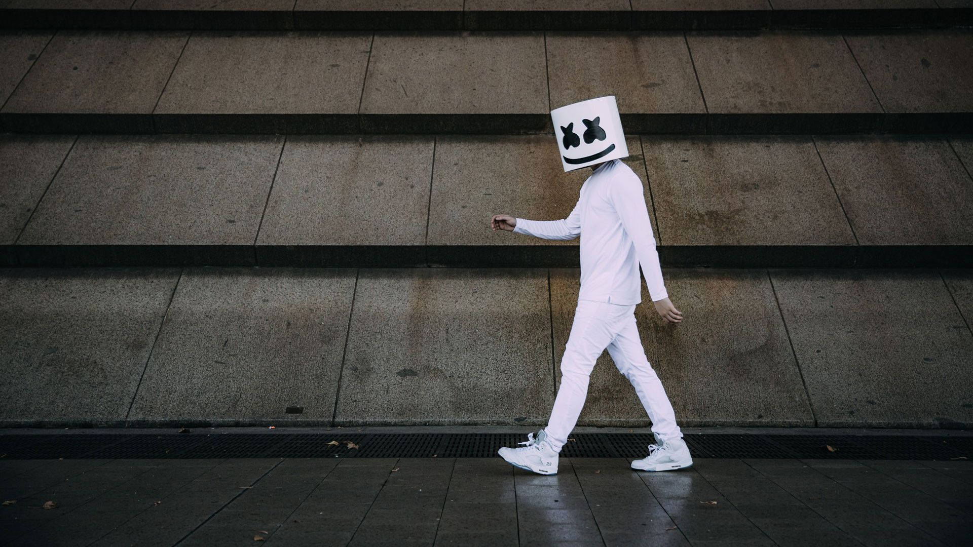 Marshmallow Dj 桌布 壁紙 — 一個戴著白色Marshmello面具、身穿全白服裝的人，在都市環境中走下混凝土階梯。