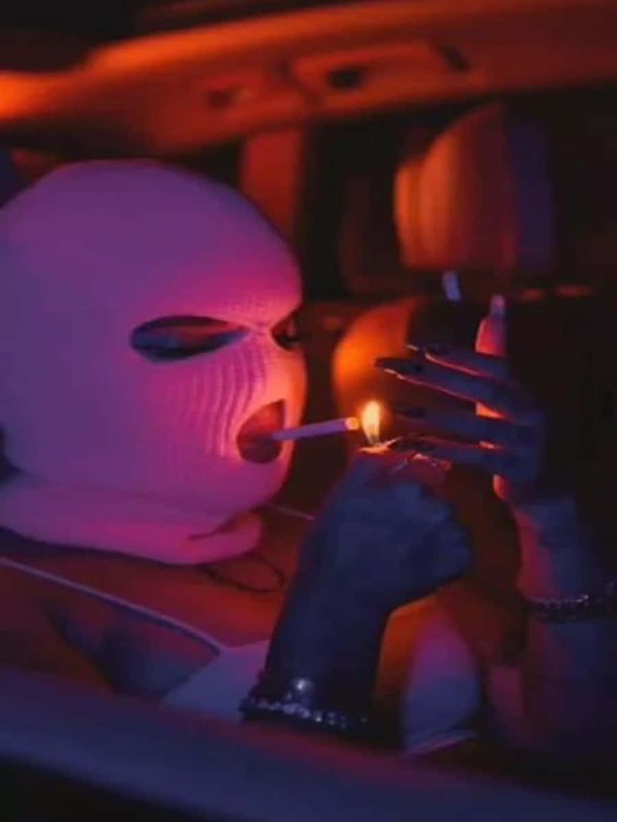Ski Mask Girl 桌布 壁紙 — 一個戴著白色滑雪面罩的人在車內點燃香煙，車內充滿粉紅和橙色的霓虹光芒。