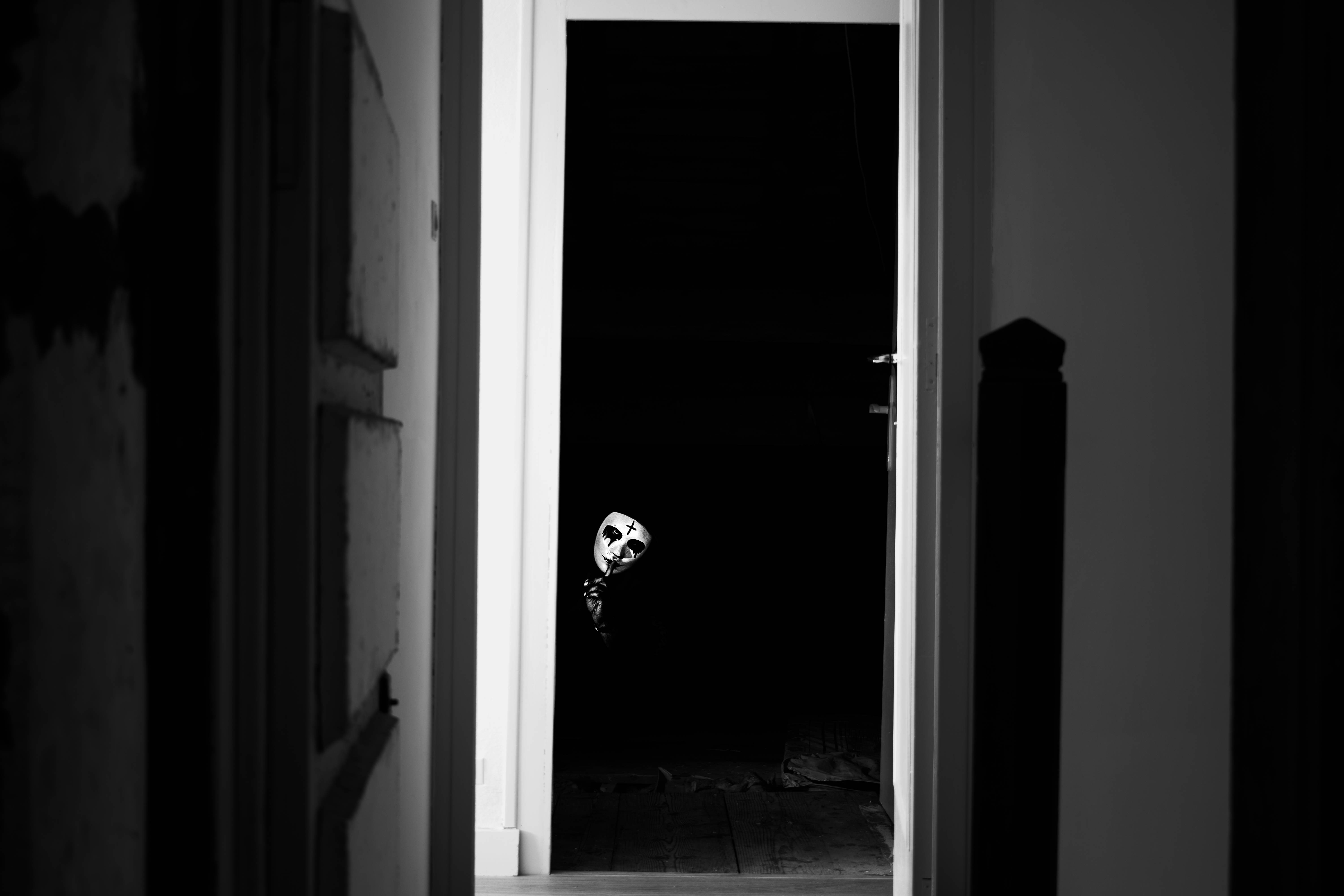 Paranormal 桌布 壁紙 — 一個戴著白色面具的人物從一個由純白飾邊框著的黑暗門口窺視，在單色走廊中。