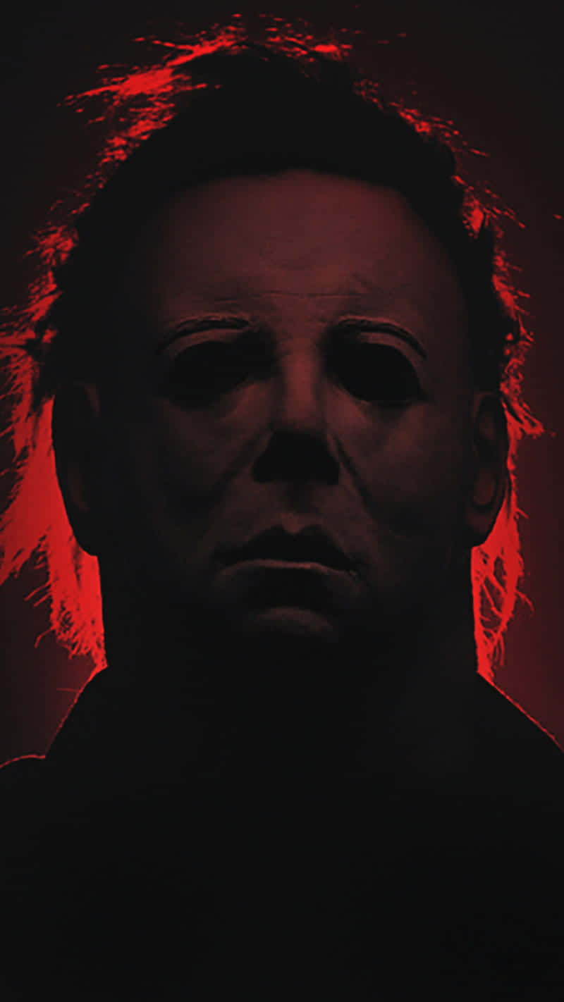 Halloween Michael Myers 桌布 壁紙 — 一個戴著白色面具的威脅人物，在黑暗背景中散發出詭異的紅光。
