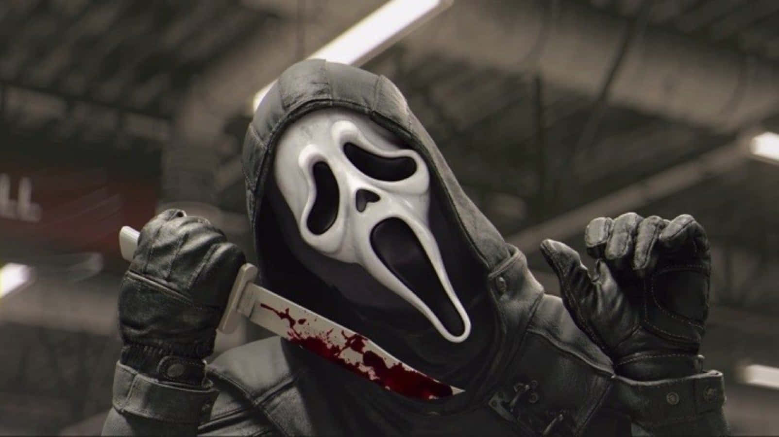 Ghostface Aesthetic 桌布 壁紙 — 一個戴著白色鬼面具、身穿黑色連帽衫的威脅人物，在昏暗的工業環境中握著一把血淋淋的刀。