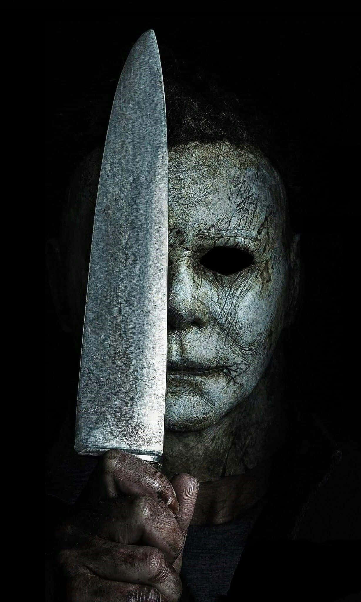 Mike Myers 桌布 壁紙 — 一個戴著破舊白色面具的威脅人物，在黑色背景前拿著一把大刀。