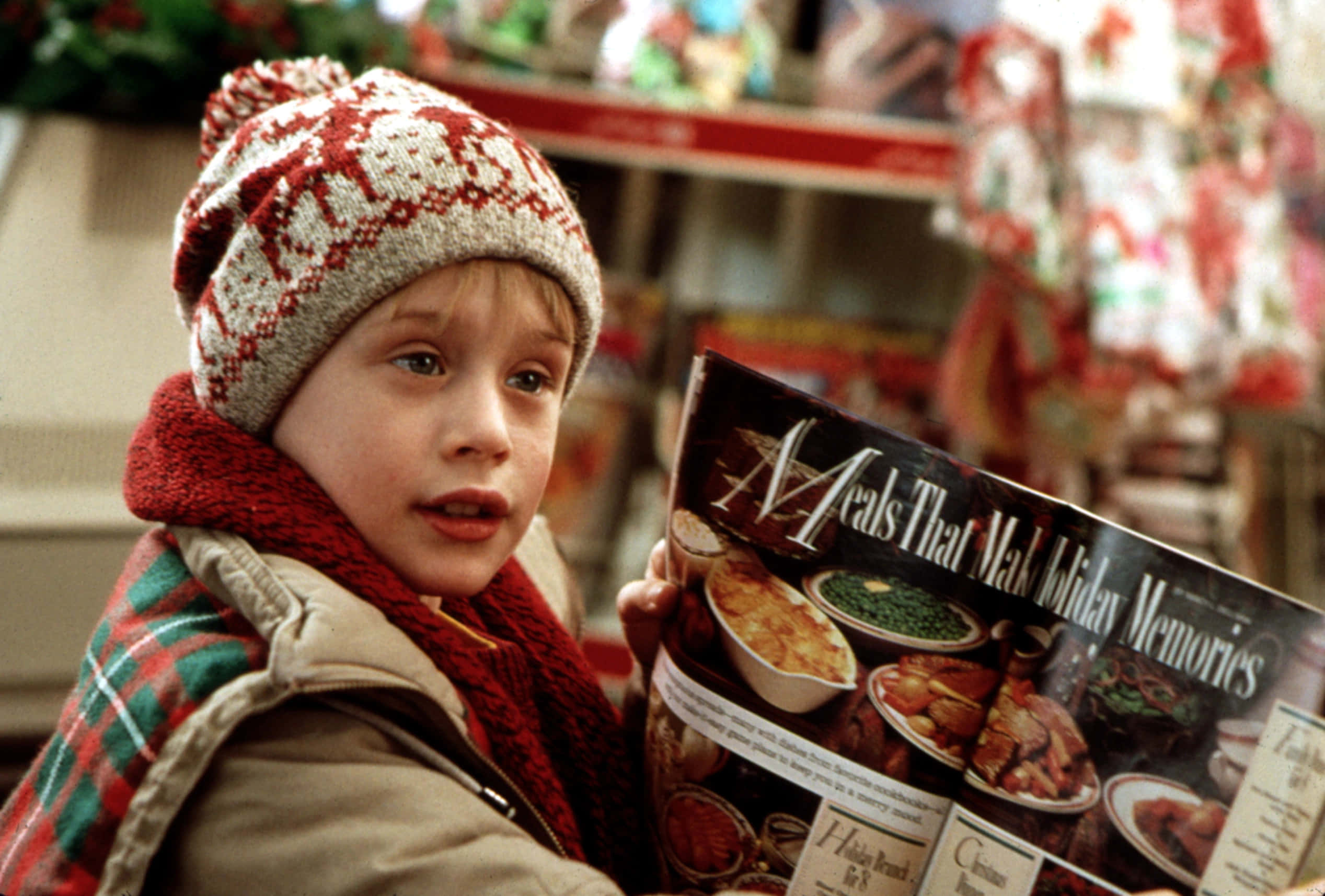Home Alone 桌布 壁紙 — 一個戴著節日針織帽和圍巾的小男孩，在溫暖燈光的商店裡若有所思地看著一本節日食譜。