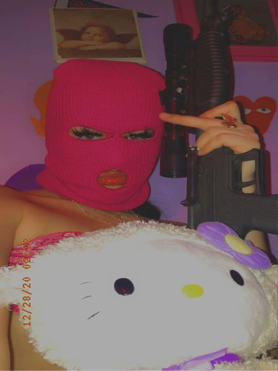 Ski Mask Girl 桌布 壁紙 — 一個戴著粉紅色巴拉克拉法帽的人，靠著紫色牆上的Hello Kitty絨毛玩具，手持步槍。