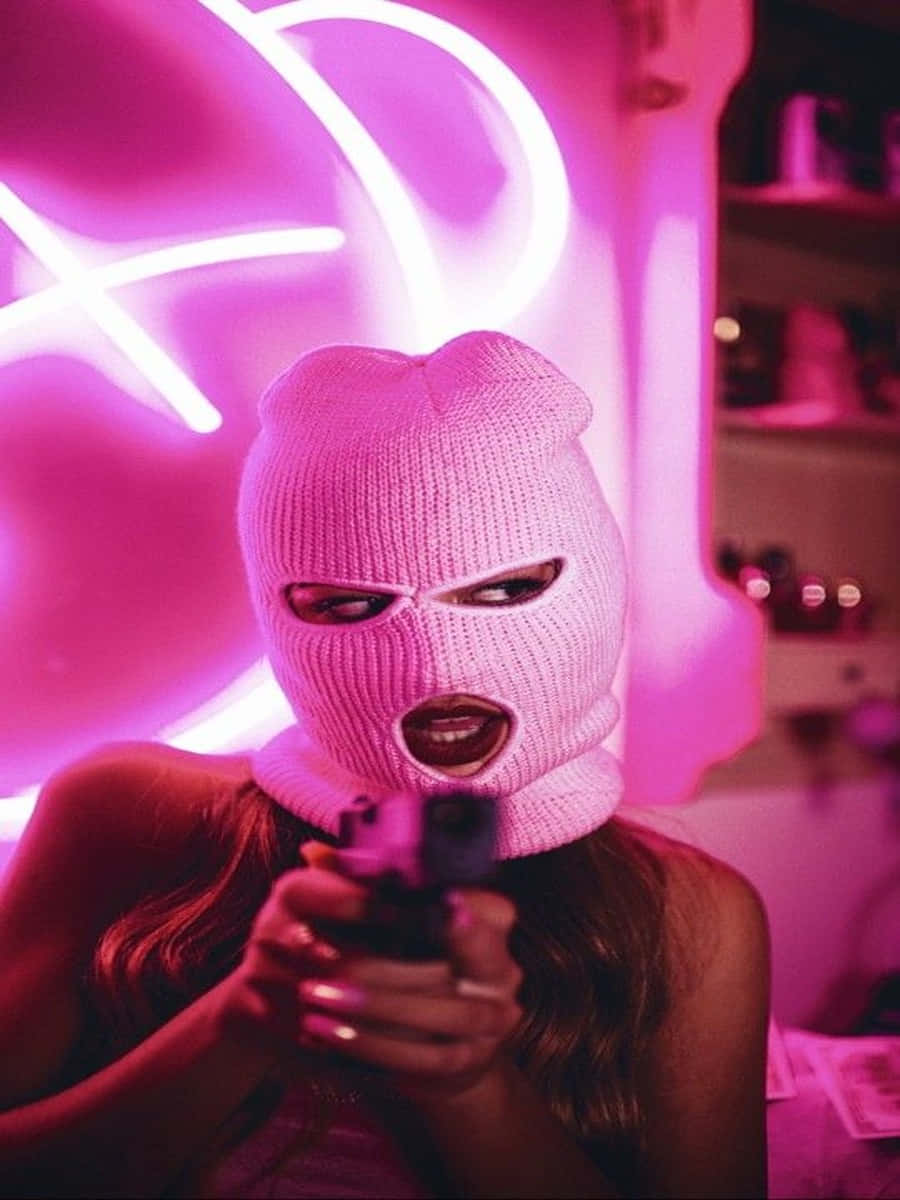 Ski Mask Girl 桌布 壁紙 — 一個戴著粉紅色針織巴拉克拉法帽的人，在昏暗的房間裡，在發光的粉紅色霓虹燈下拿著槍。