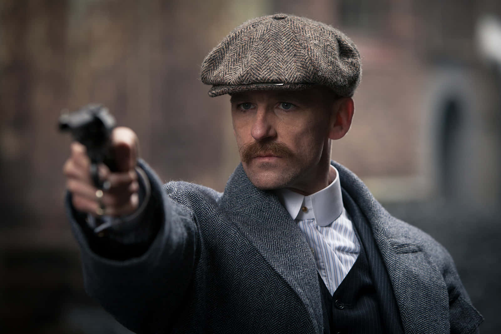 穿著復古外套和帽子的男人，表情嚴肅地瞄準手槍。 — Peaky Blinders 壁紙