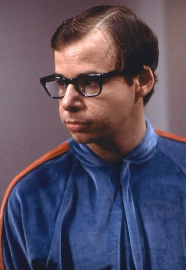 rick moranis 桌布 壁紙 — 一個戴著粗黑框眼鏡、身穿藍色天鵝絨運動服的男人，表情嚴肅地望向一旁。