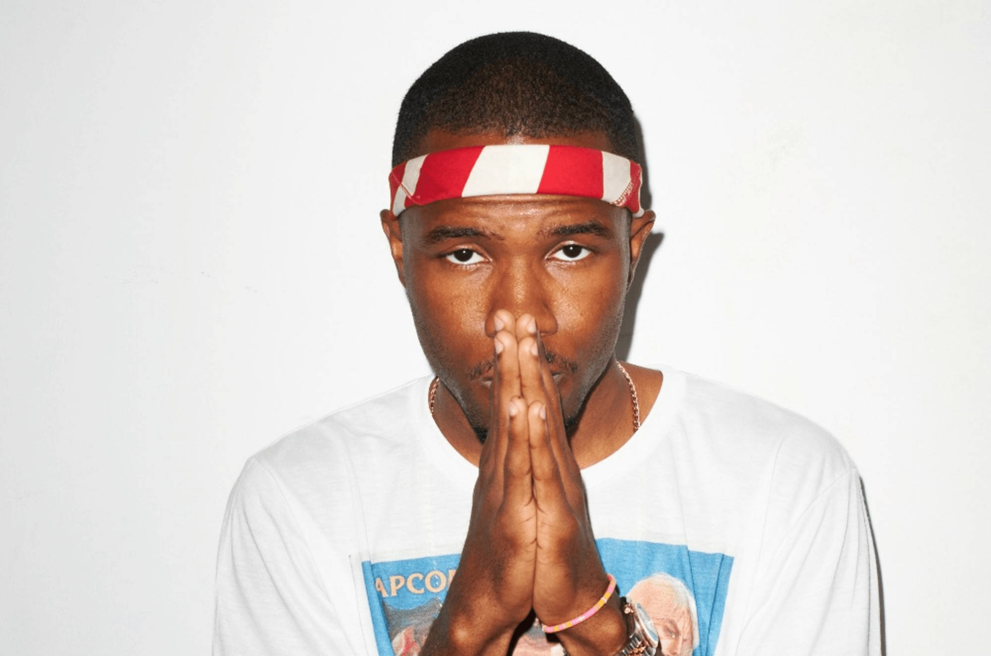 Frank Ocean 桌布 壁紙 — 一個戴著紅白條紋頭帶的男人，在純白背景前將雙手合十放在臉前。