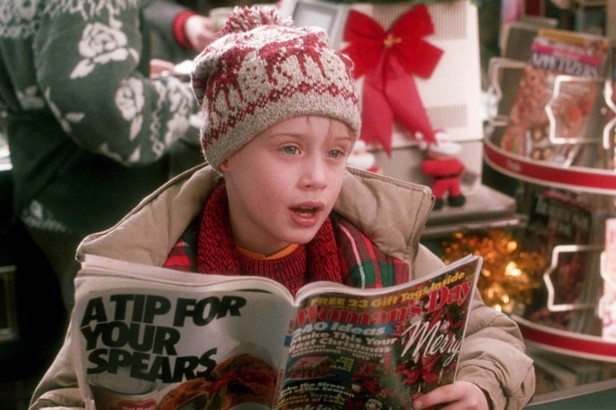 Home Alone 桌布 壁紙 — 一個戴著紅白針織帽和圍巾的小男孩，在節日佈置中帶著驚訝的表情閱讀雜誌。