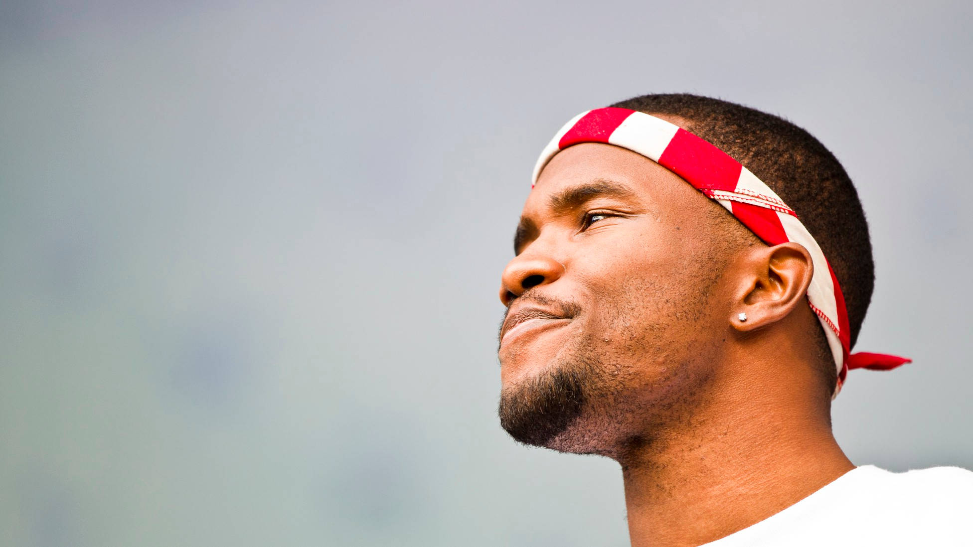 Frank Ocean 桌布 壁紙 — 一個戴著紅白頭帶的男人，在柔和的灰色天空下，帶著平靜的表情向上凝視。