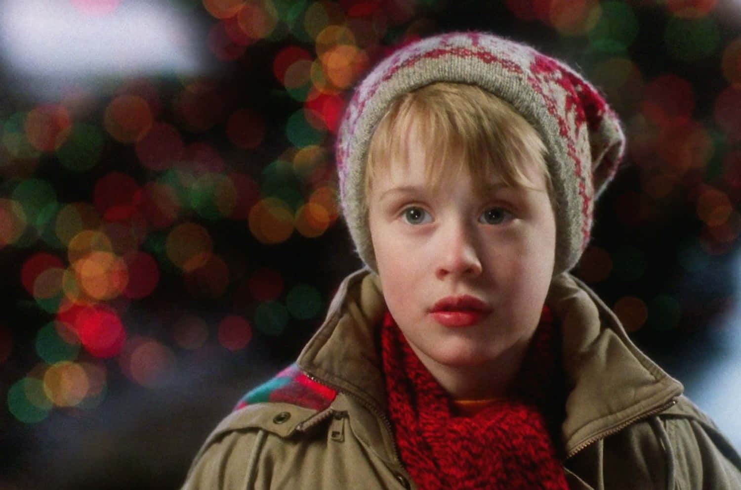 Home Alone 桌布 壁紙 — 一個戴著紅色圍巾和圖案帽子的年輕男孩，在節日散景燈光的背景下莊嚴地凝視。