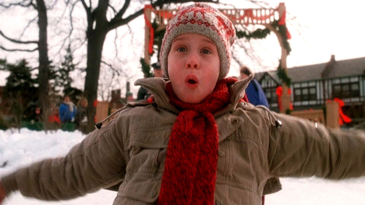 Home Alone 桌布 壁紙 — 一個戴著紅色圍巾和針織帽、睜大眼睛的孩子，站在白雪皚皚的冬季仙境中，雙臂張開，充滿驚喜。