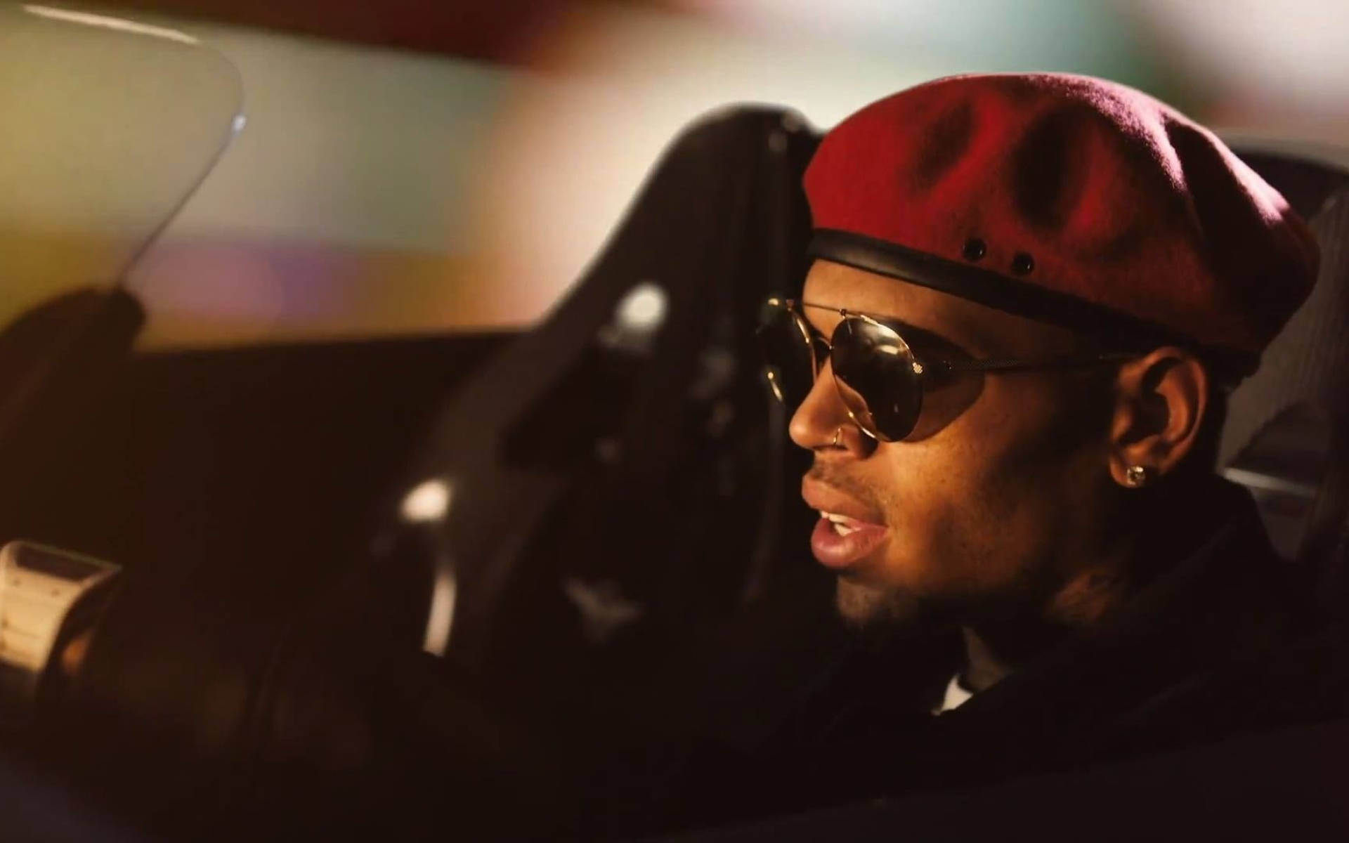 Chris Brown 桌布 壁紙 — 一個戴著紅色貝雷帽和金色邊框太陽眼鏡的男人自信地坐在一輛時尚跑車內，背景是夜晚模糊的城市燈光。