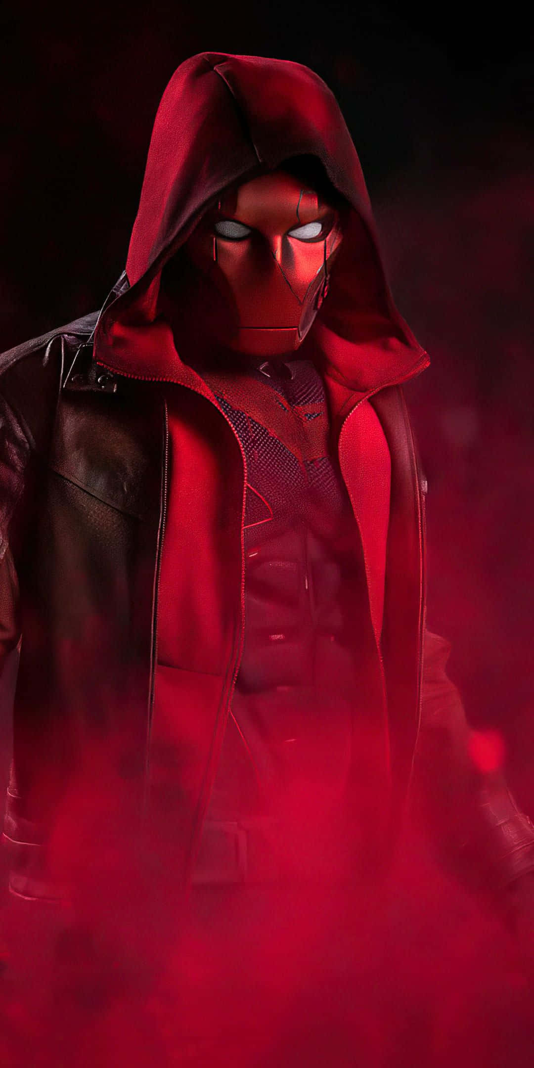 Batman Under The Red Hood 桌布 壁紙 — 一個戴著紅色面具、身穿連帽外套的超級英雄，站在煙霧瀰漫的紅光中，眼睛發光，身穿皮夾克。
