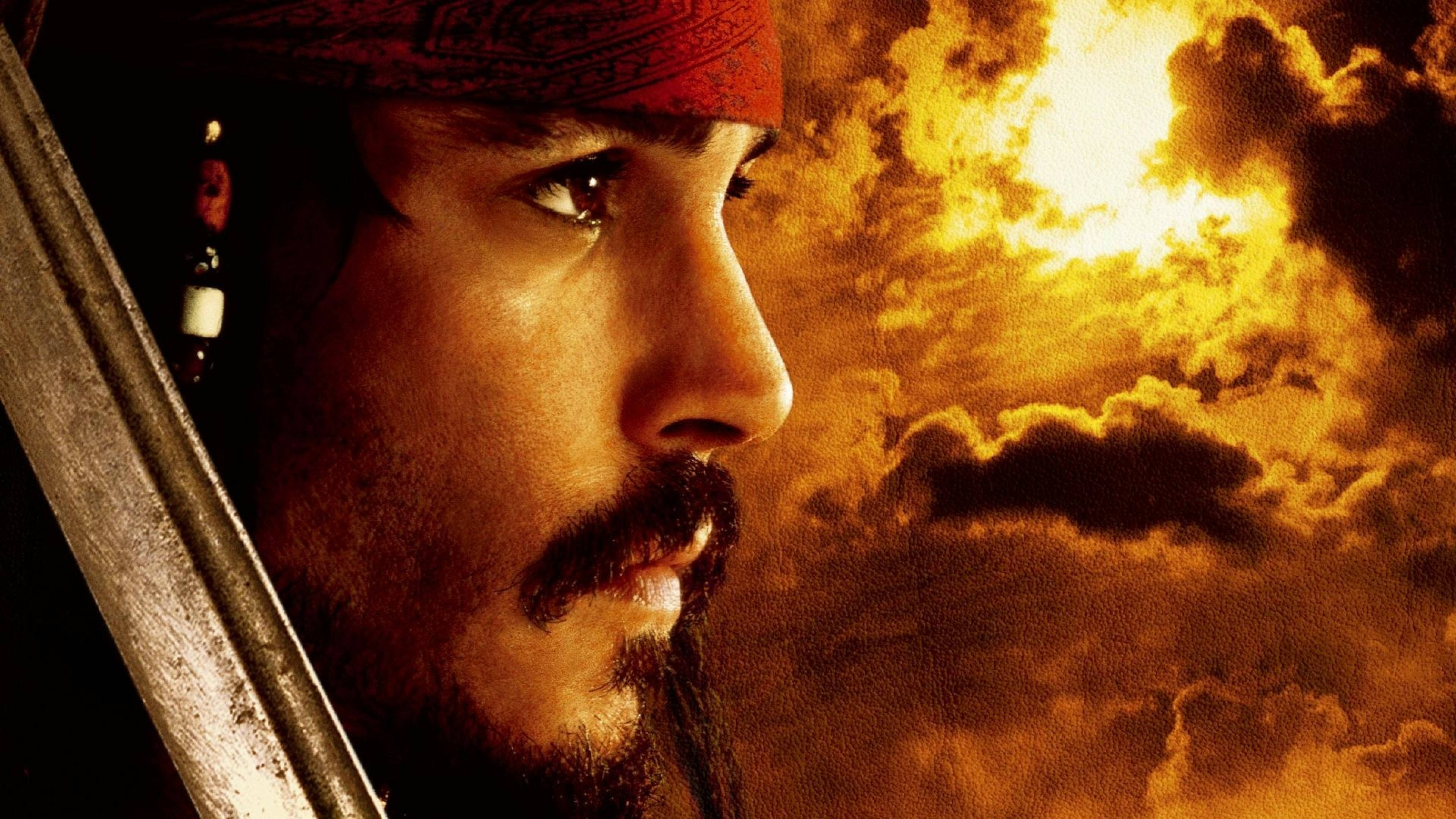 Pirates Of The Caribbean 桌布 壁紙 — 一個戴著紅色頭巾、手持劍的海盜，專注地凝視著熾熱的日落天空。