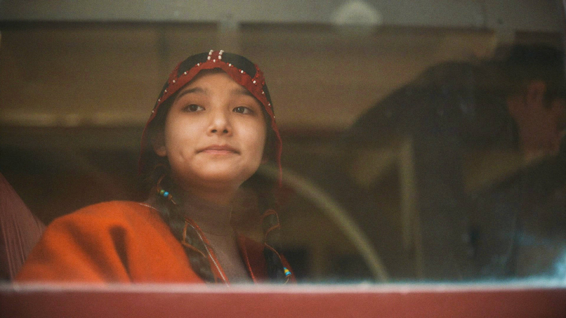 E 桌布 壁紙 — 一個戴著紅色頭飾、身穿橙色衣服的小女孩，從車內透過微微起霧的車窗若有所思地凝視著。