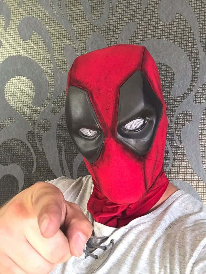 Deadpool Mask 桌布 壁紙 — 一個戴著紅黑色死侍面具的人直接指向鏡頭，背景是灰色圖案壁紙。
