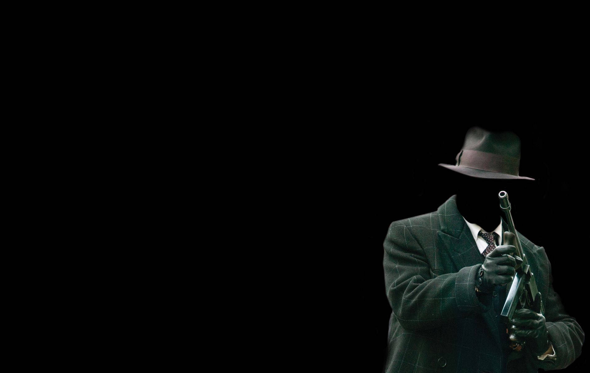 Mafia 桌布 壁紙 — 一個戴著紳士帽、身穿西裝的神秘身影，在純黑背景下手持手槍。