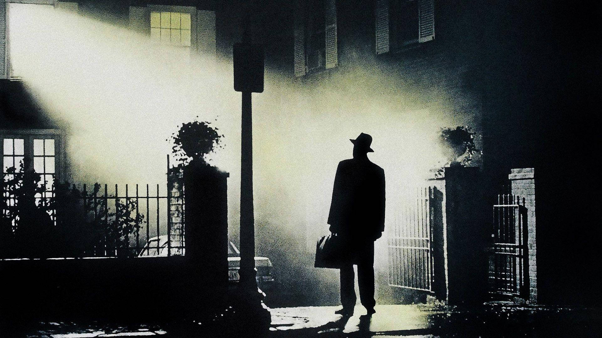 Exorcist 桌布 壁紙 — 一個戴著紳士帽和穿著風衣的孤獨男子，在夜晚霧氣瀰漫的城市小巷中形成剪影，沐浴在戲劇性的背光中。