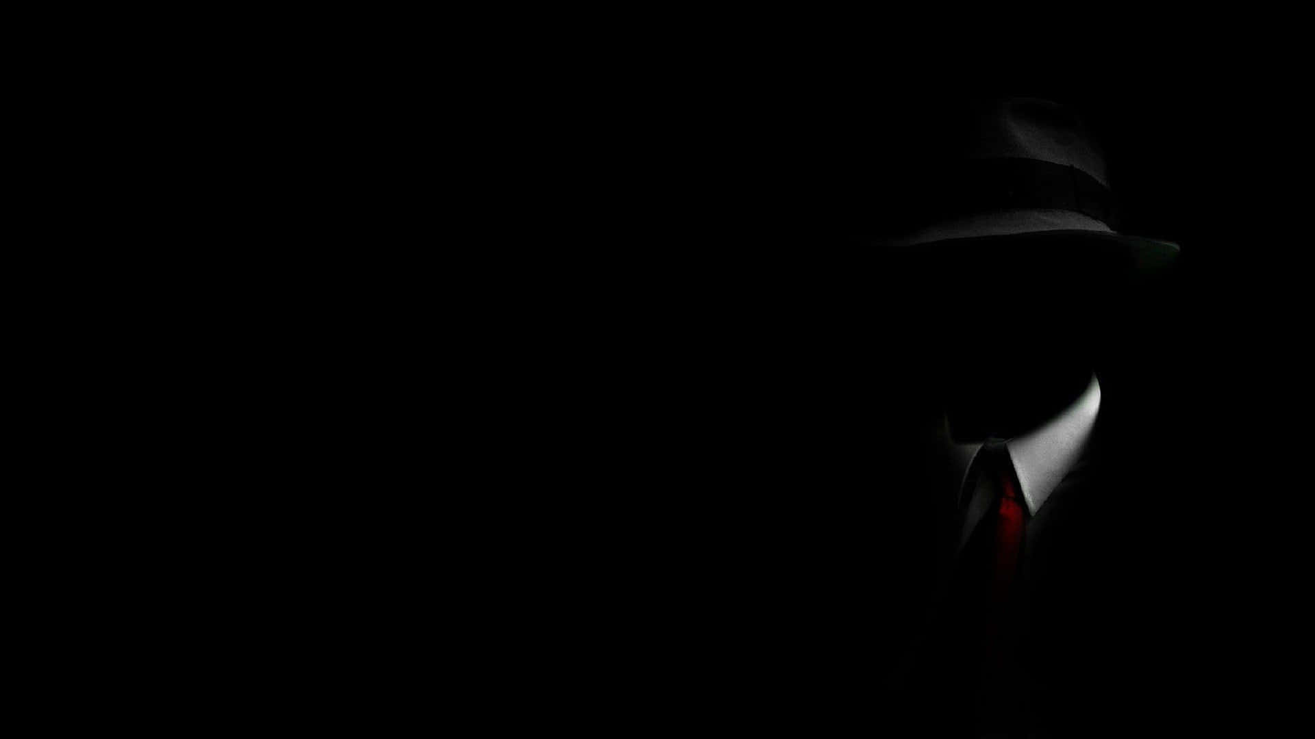 Mafia 桌布 壁紙 — 一個戴著紳士帽和紅色領帶的陰影人物從黑暗中浮現，只有白色領口被照亮。