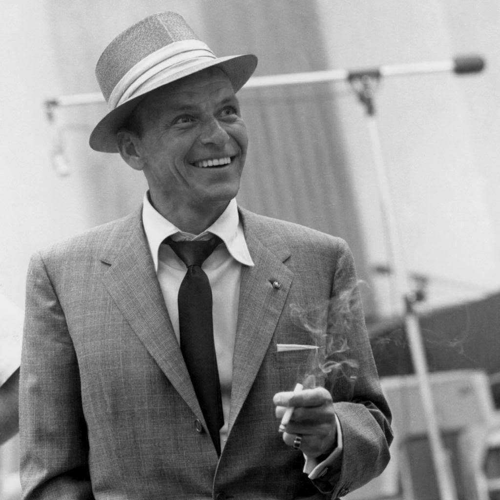Sinatra 桌布 壁紙 — 一個戴著紳士帽和西裝的微笑男人手持香煙，煙霧向上繚繞，是一張復古黑白照片。