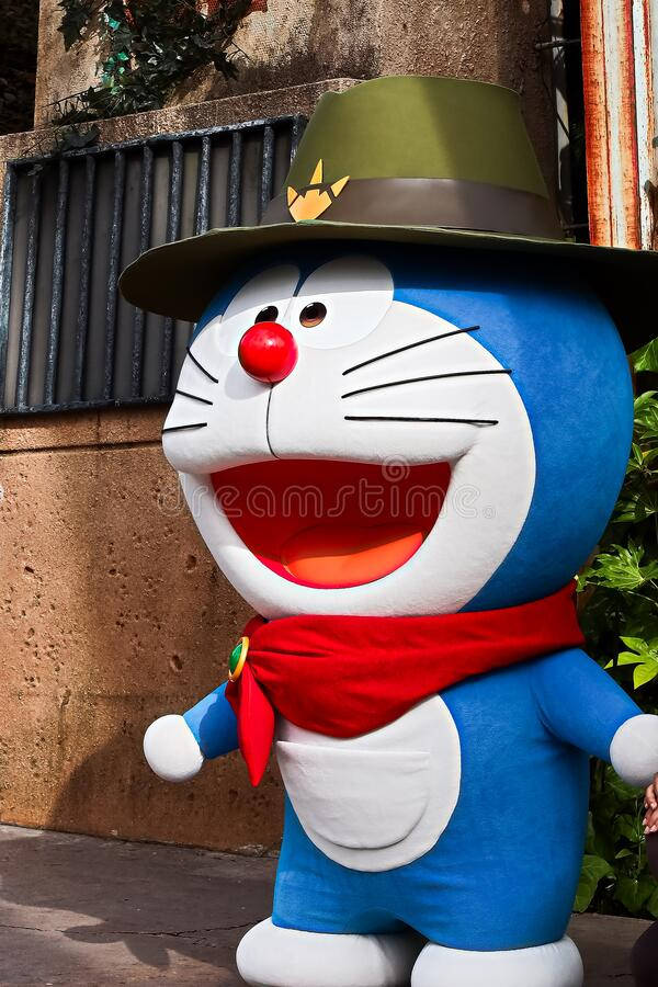 doraemon 4K 桌布 壁紙 — 一個戴著綠色帽子和紅色圍巾的開心藍色卡通角色，在有紋理的牆壁前微笑站立在戶外。
