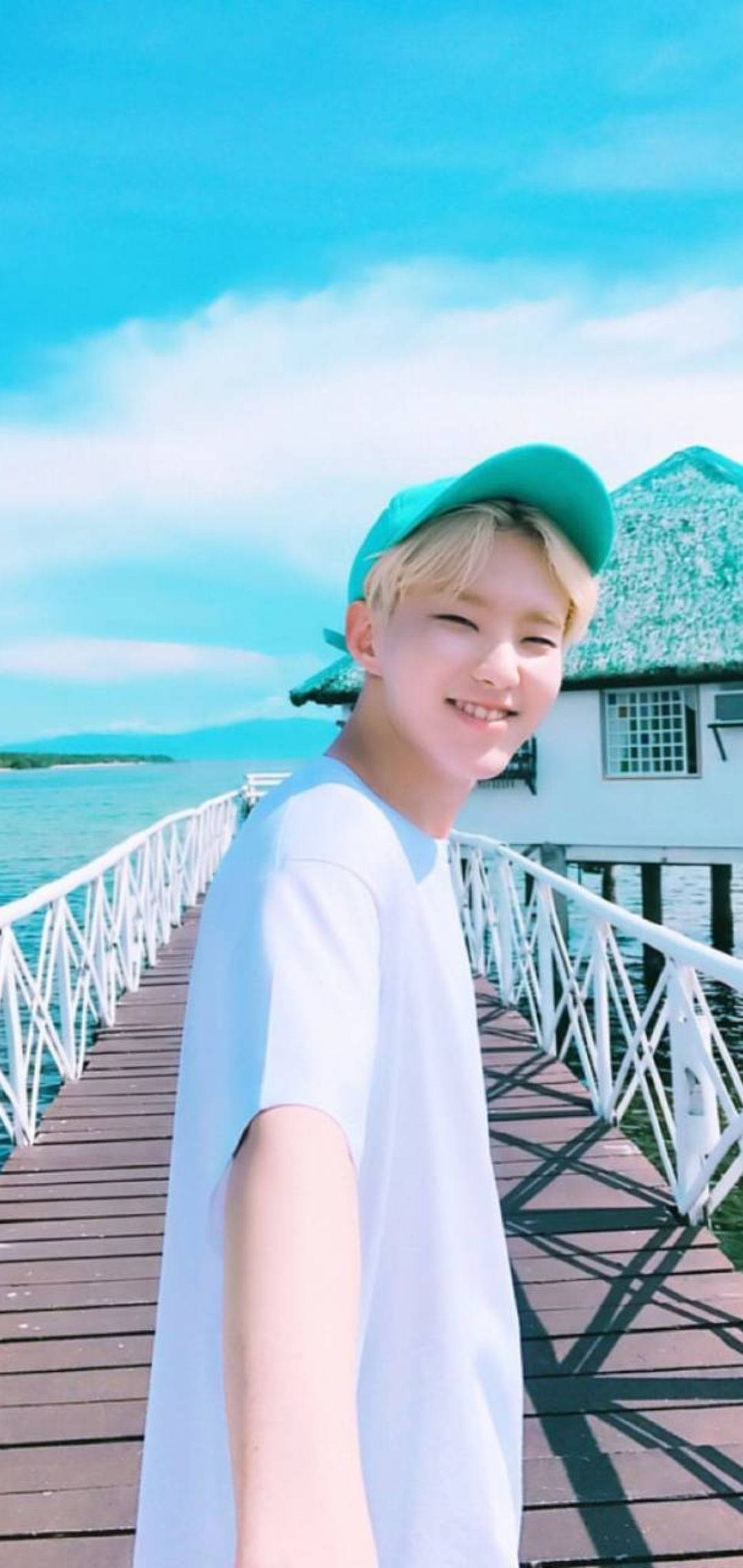 Hoshi 桌布 壁紙 — 一個戴著綠色帽子的微笑年輕人在木製碼頭上俯瞰著碧綠色的海水，天空湛藍。
