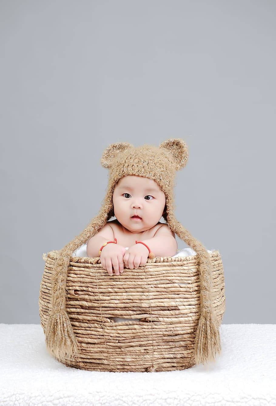 Baby Boy 桌布 壁紙 — 一個戴著編織熊帽的嬰兒坐在藤籃裡，背景是柔和的灰色。