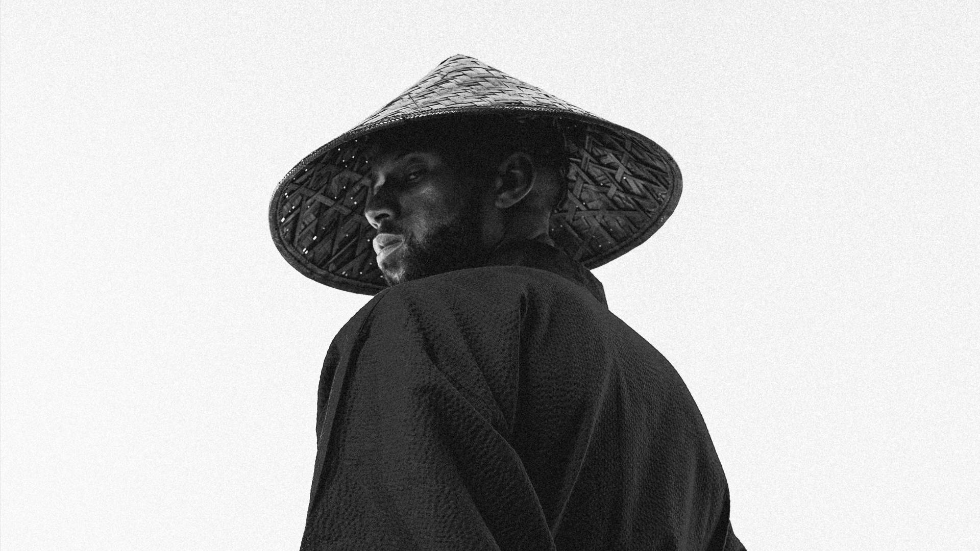 足球 桌布 壁紙 — 一個戴著編織錐形帽和深色長袍的男人，在純白背景上轉頭越過肩膀。