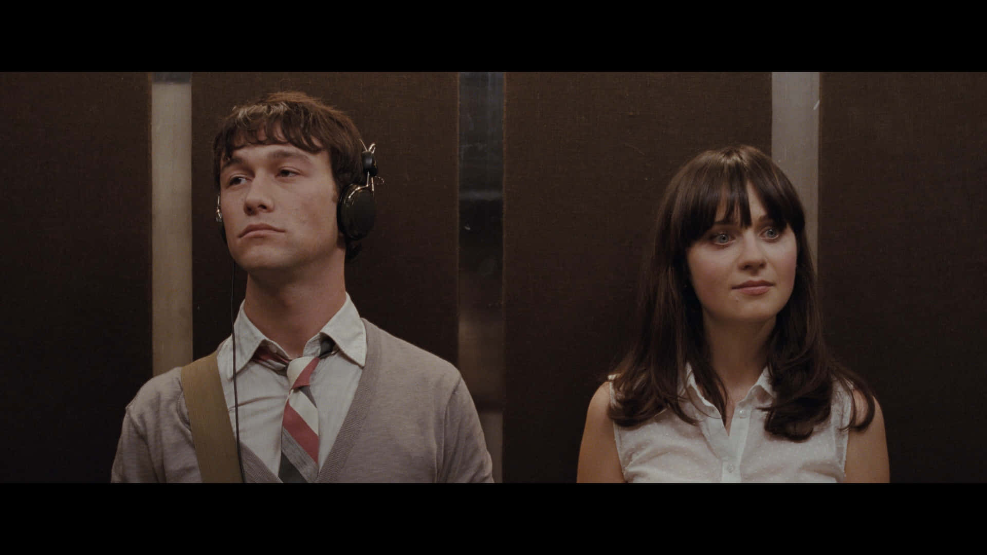 500 Days Of Summer 桌布 壁紙 — 一個戴著耳機的男人和一個女人沉默地站在昏暗的電梯裡，他們的表情緊張而疏遠。