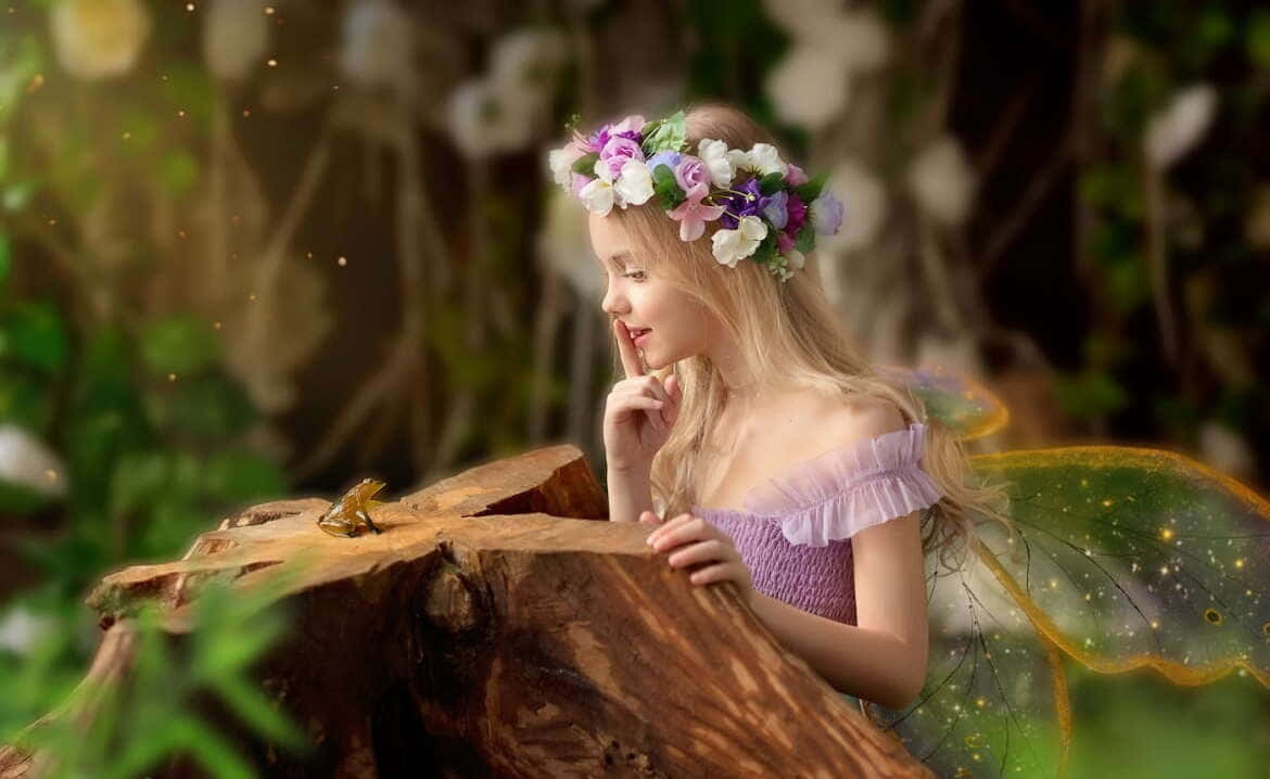 仙女 桌布 壁紙 — 一個戴著花冠、擁有發光翅膀的年輕女孩，在陽光斑駁的森林中，對著棲息在長滿苔蘚的樹樁上的青蛙低聲訴說秘密。