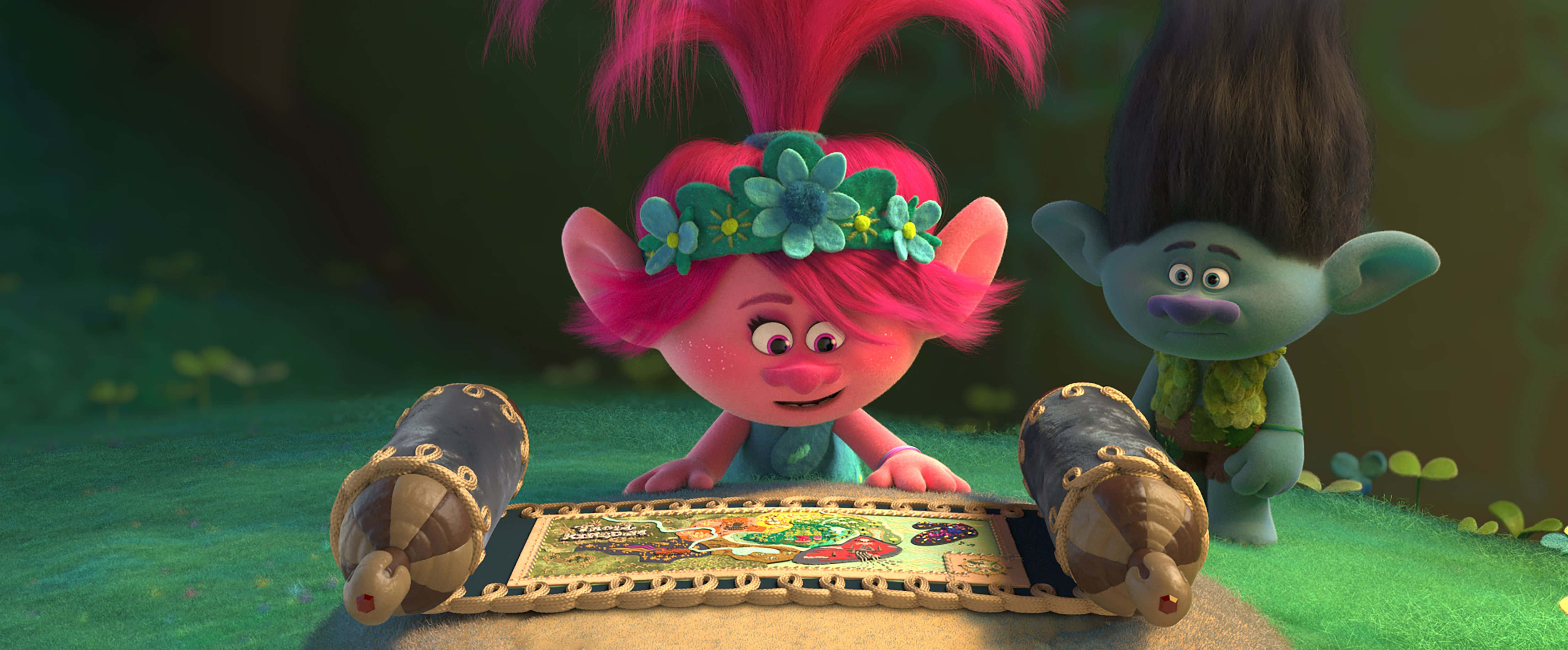 Trolls World Tour 桌布 壁紙 — 一個戴著花冠、粉紅色頭髮的快樂巨魔在茂密的綠色森林中窺視著一張色彩繽紛的地圖。