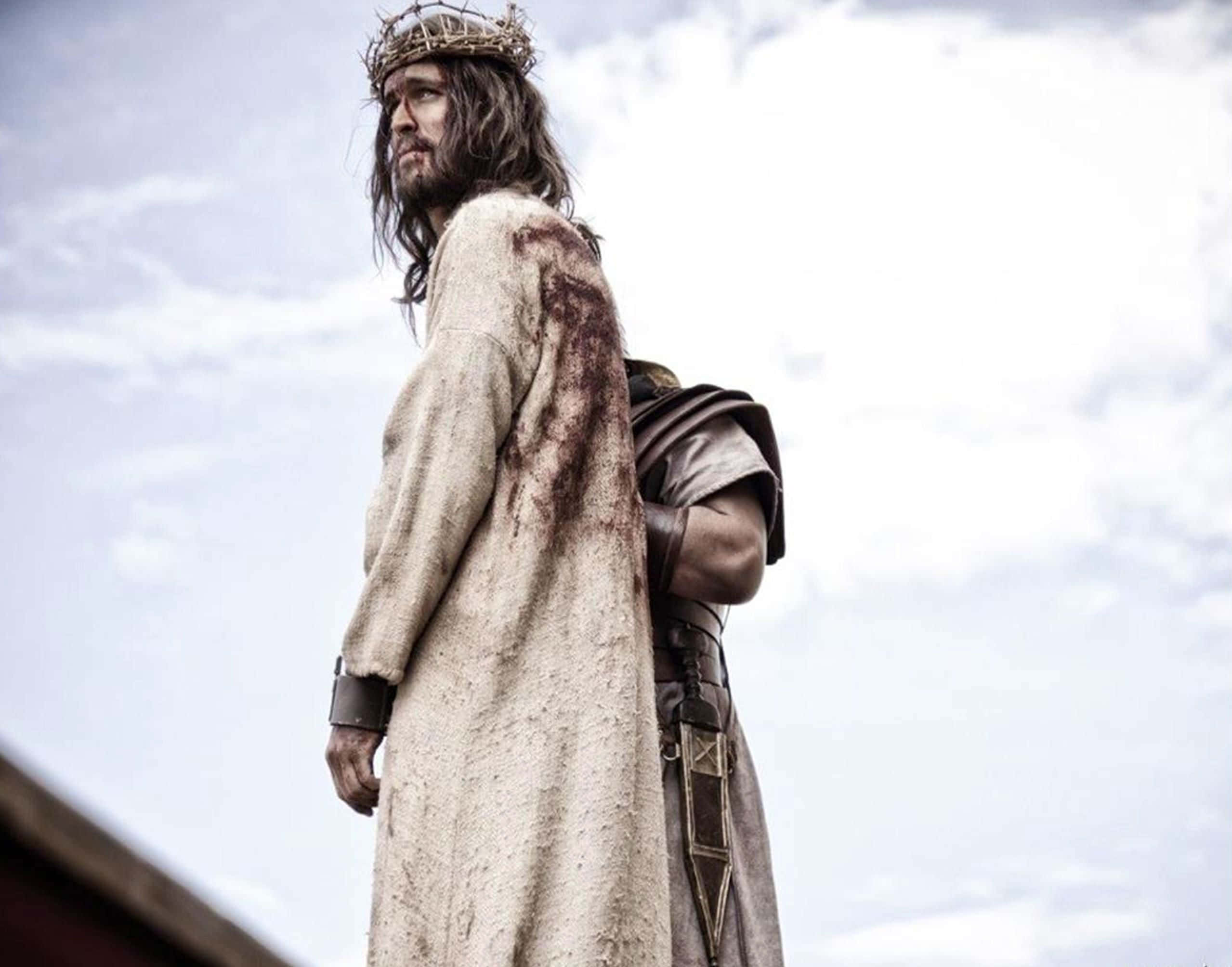 Son Of God 桌布 壁紙 — 一個戴著荊棘冠冕、身穿血跡斑斑長袍的男子，在陰雲密佈的天空下莊嚴地站立。
