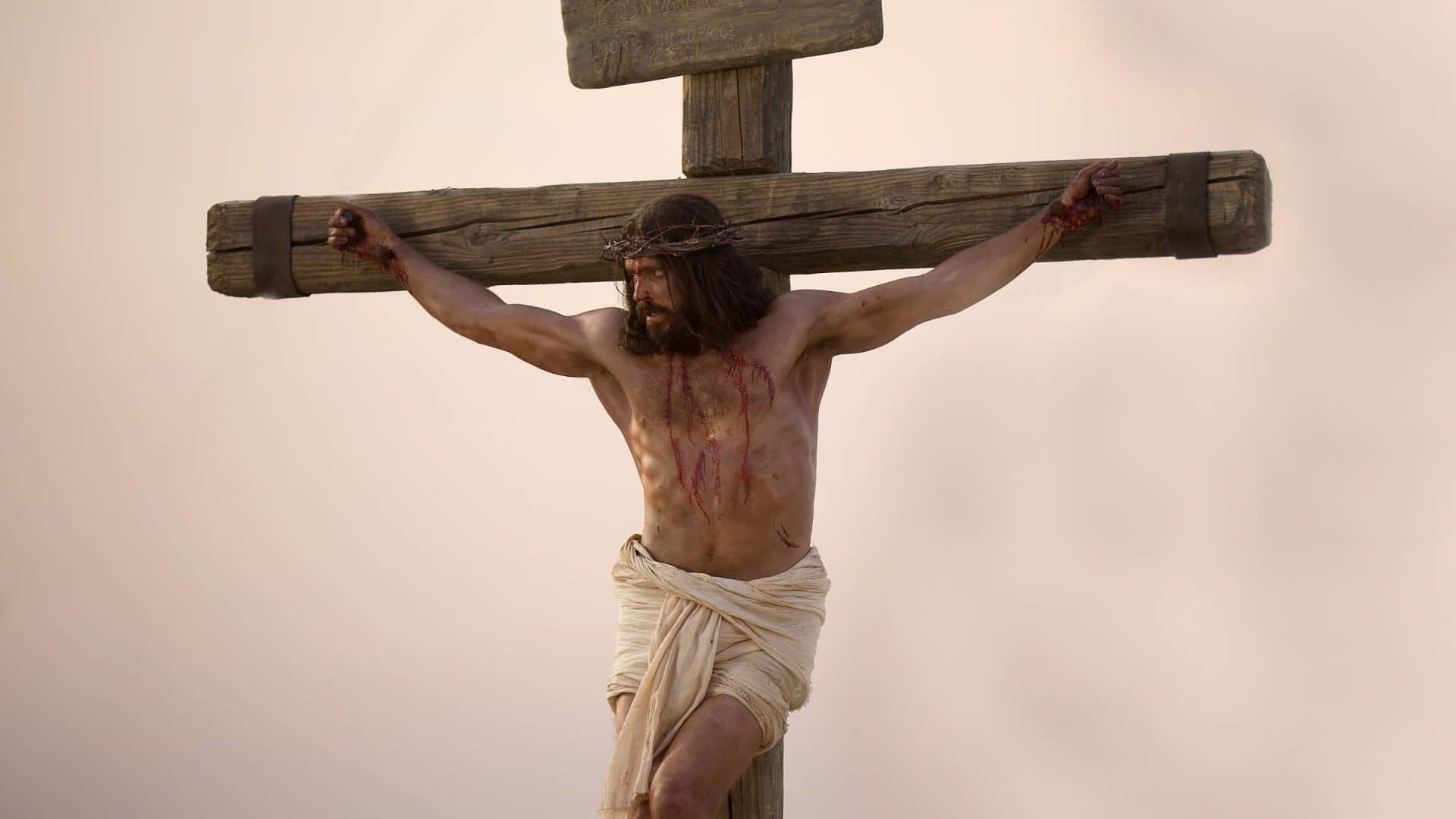Jesus Crucifixion 桌布 壁紙 — 一個戴著荊棘冠冕的男人被釘在木頭十字架上，背景是蒼白的天空。