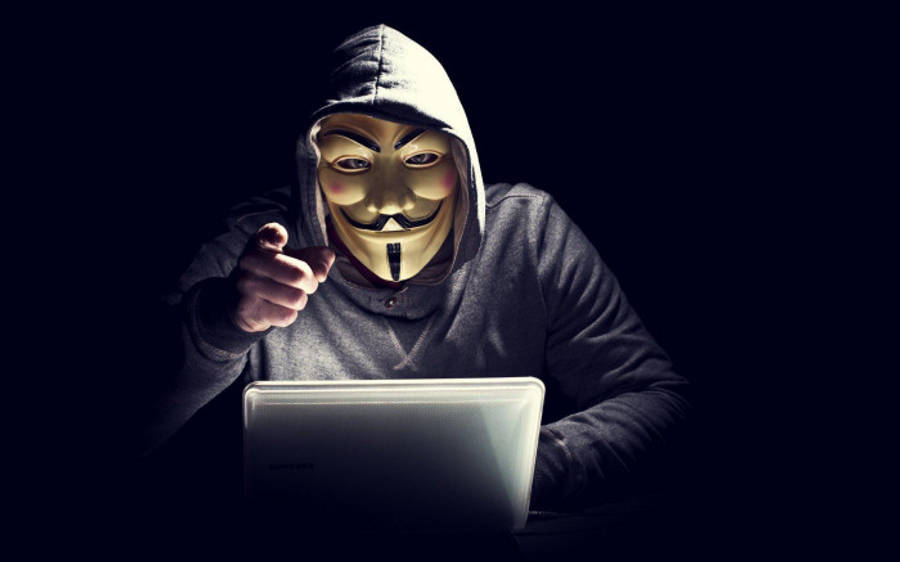 hacker 3d 桌布 壁紙 — 一個戴著蓋伊·福克斯面具和連帽衫的人在黑暗的房間裡指責性地指著一個筆記型電腦。