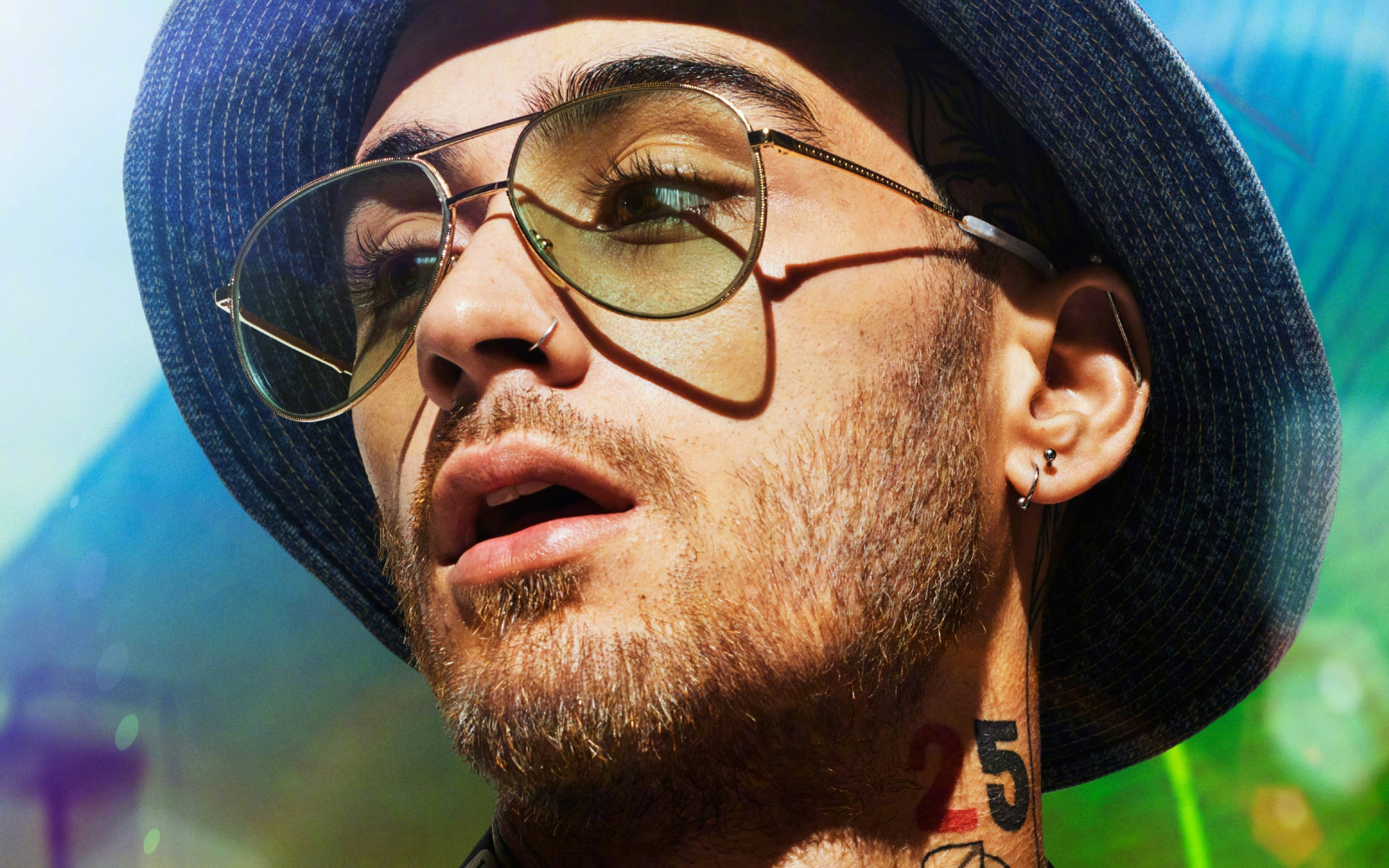 zayn 桌布 壁紙 — 一個戴著藍色帽子和飛行員太陽眼鏡的男人，在充滿活力的陽光背景和彩色散景中向上凝視。