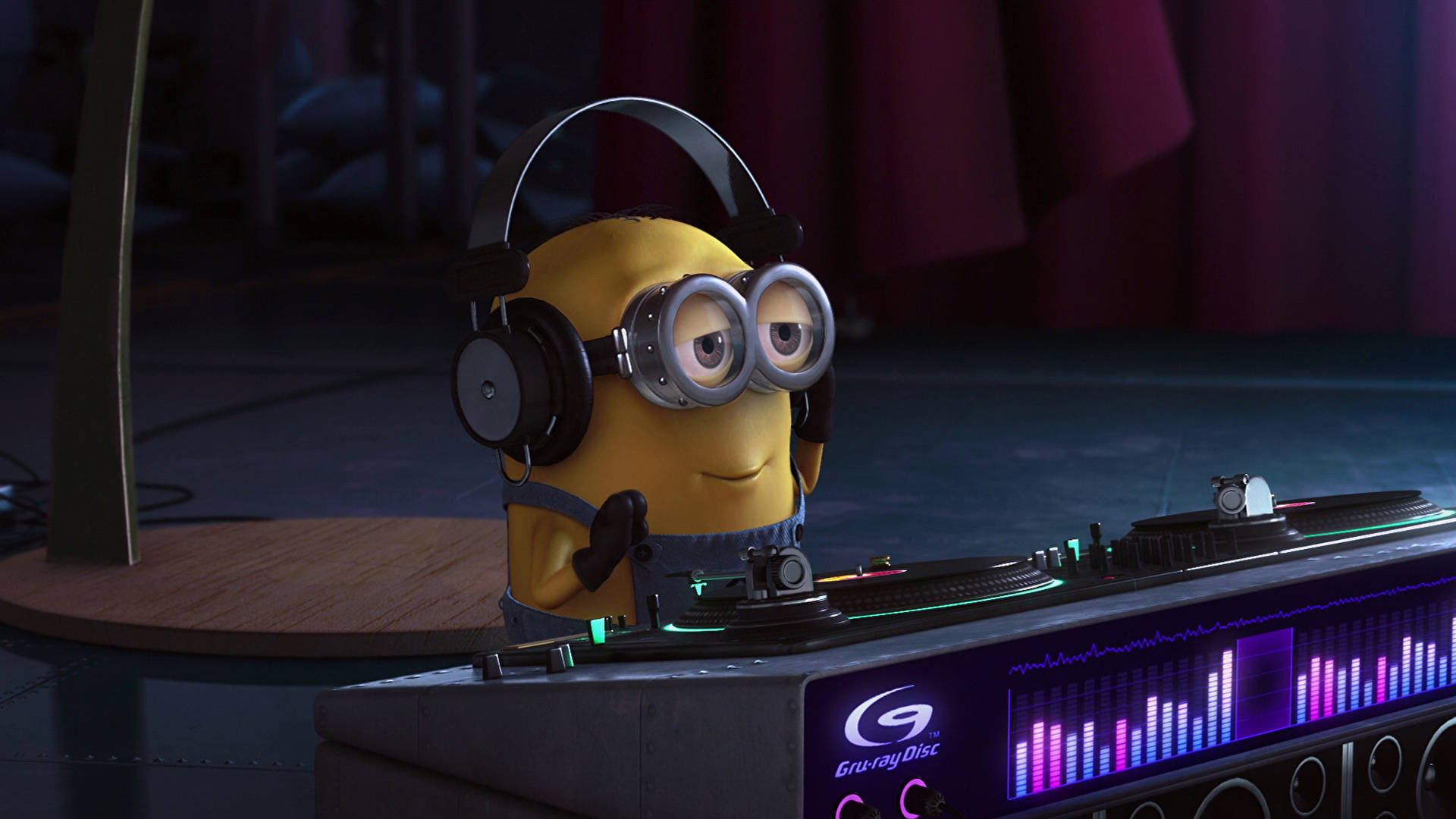 Despicable Me 2 桌布 壁紙 — 一個戴著護目鏡和耳機的黃色Minion在昏暗的舞台燈光下，在發光的DJ唱盤上混音。